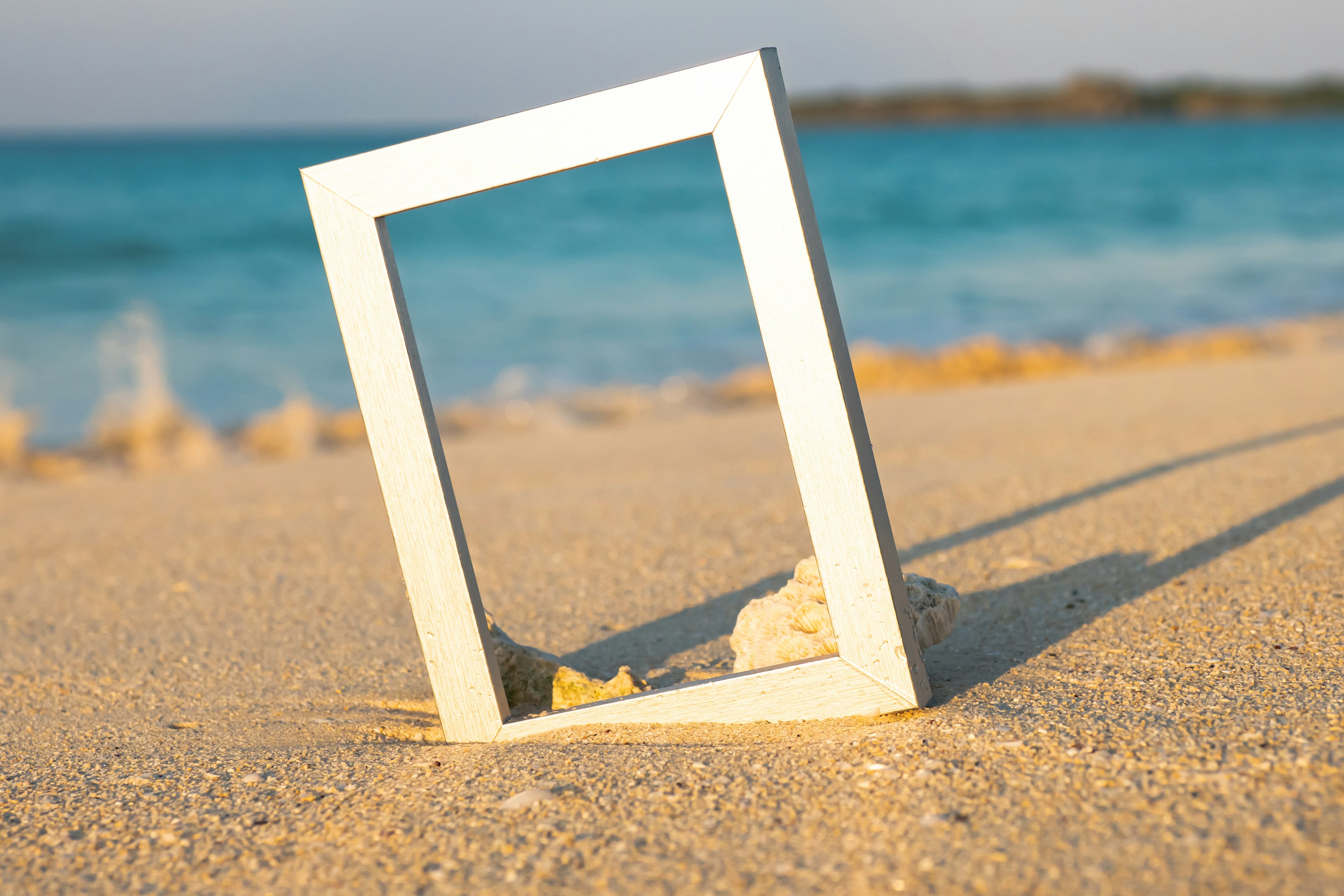 A white frame standing on sandy beach with blue ocean in the background