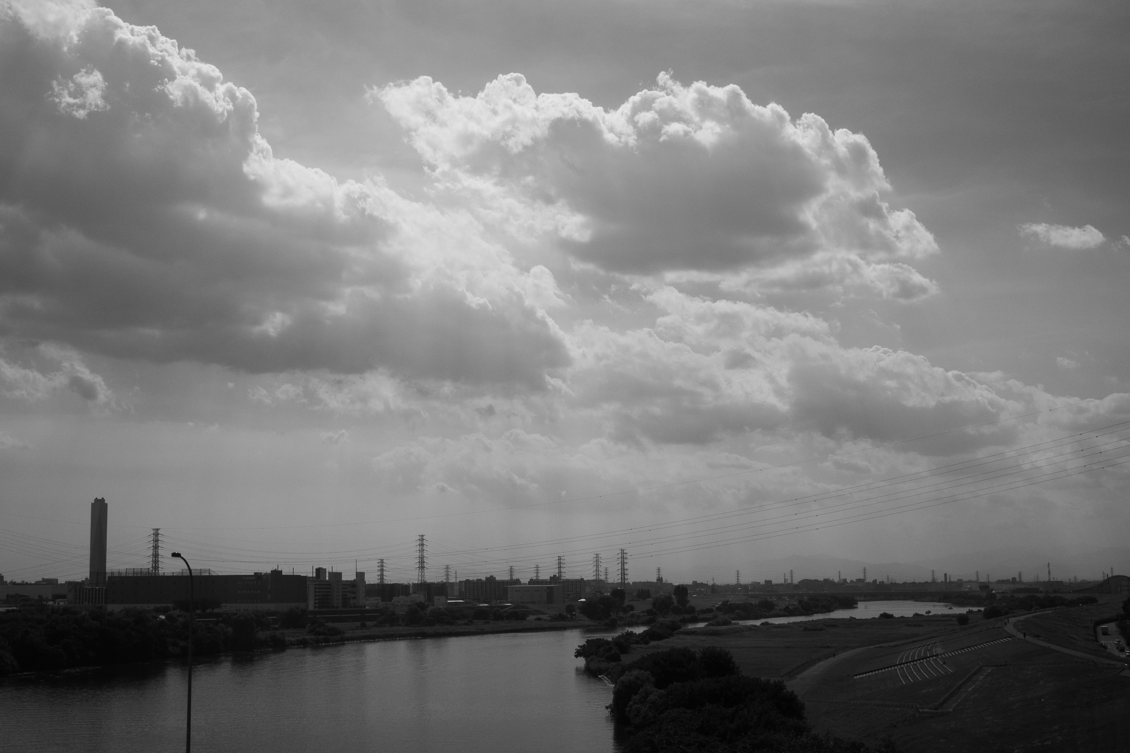 Photo de paysage en noir et blanc montrant une zone industrielle et une rivière de grands nuages remplissent le ciel