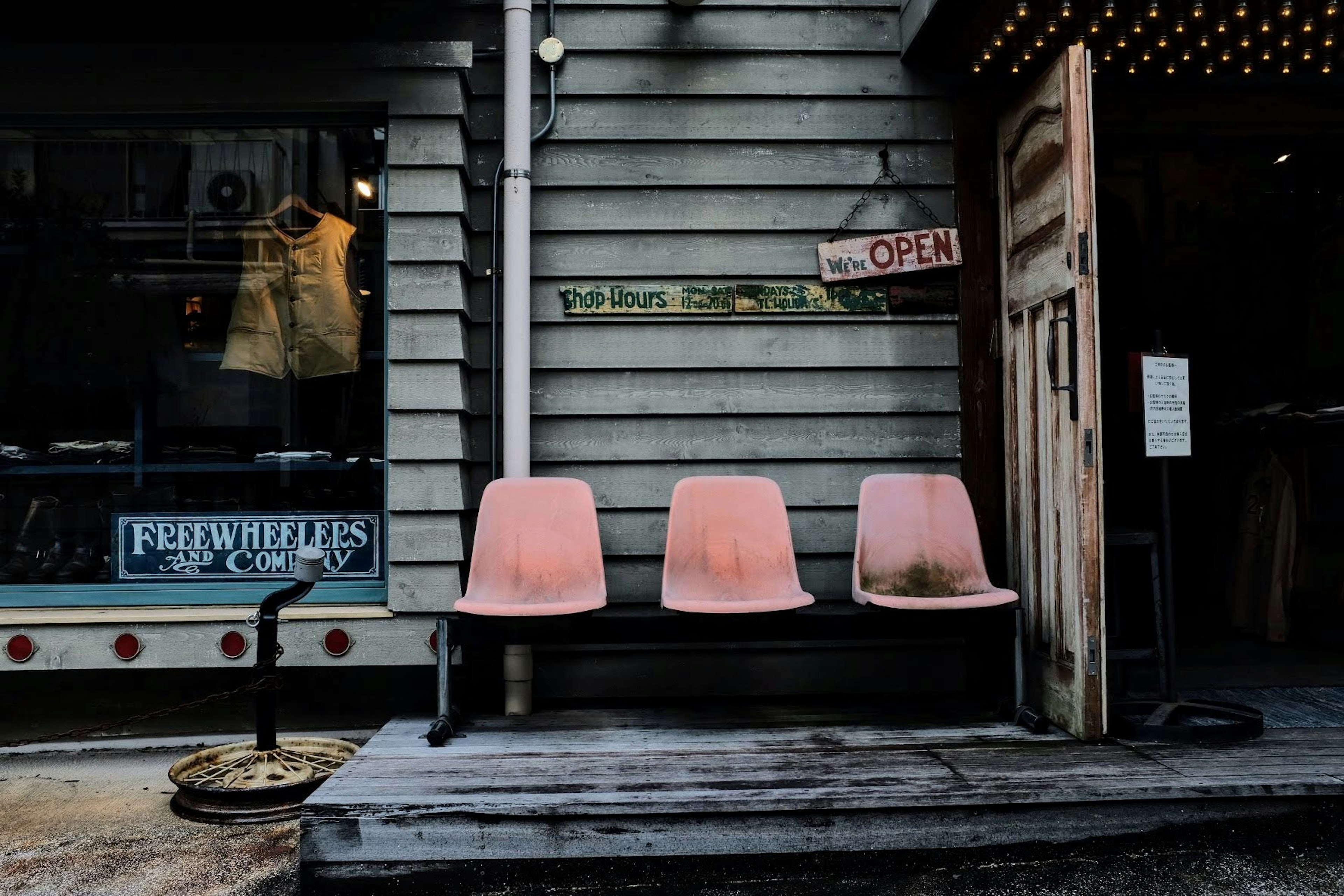 Pink chairs lined up in front of an old wooden building with an open sign