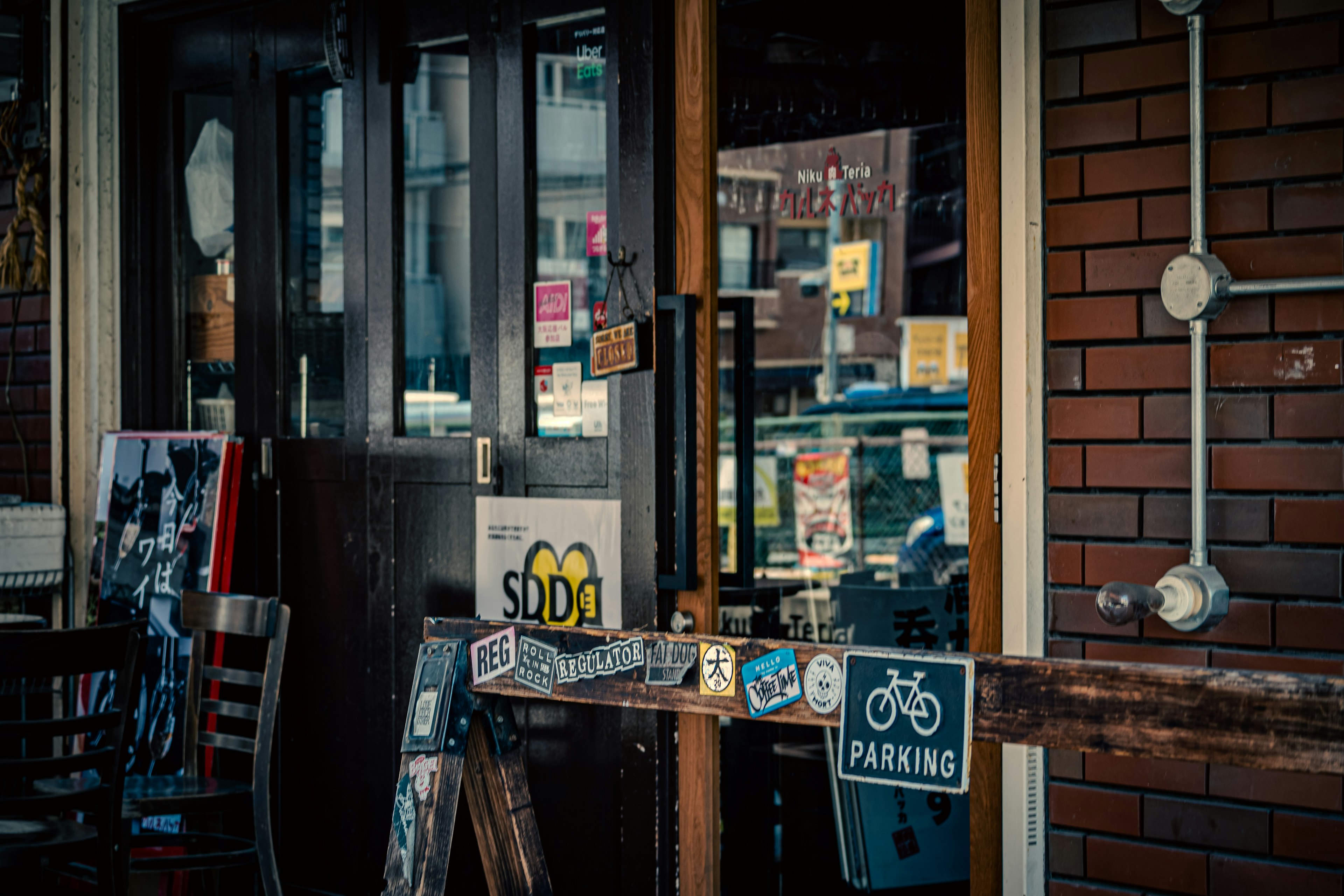 Extérieur de café avec porte en bois et mur en brique, affichant des panneaux et un panneau de stationnement pour vélos