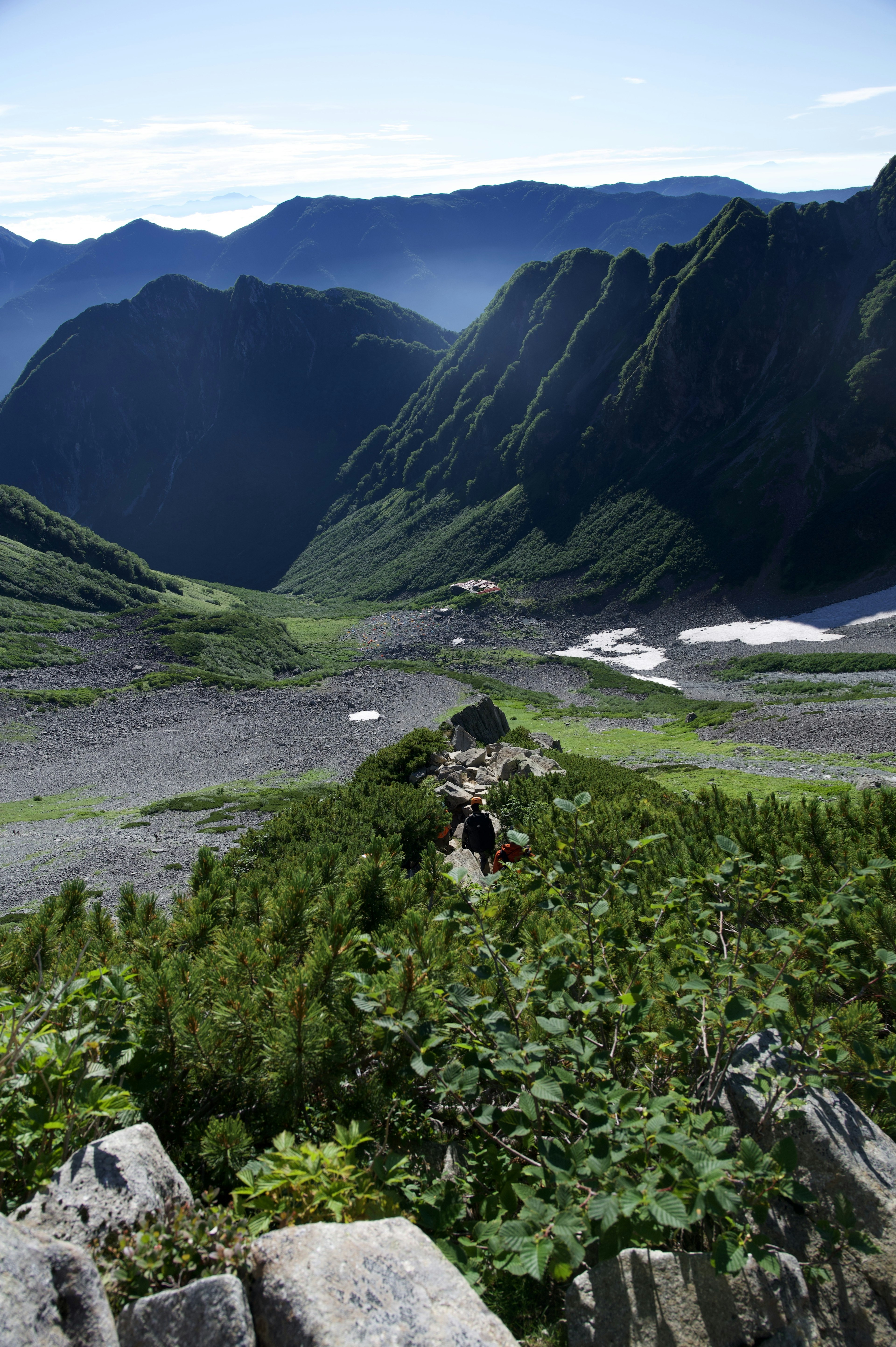 Vue panoramique d'une vallée entourée de montagnes avec de la végétation verte et des chemins rocheux