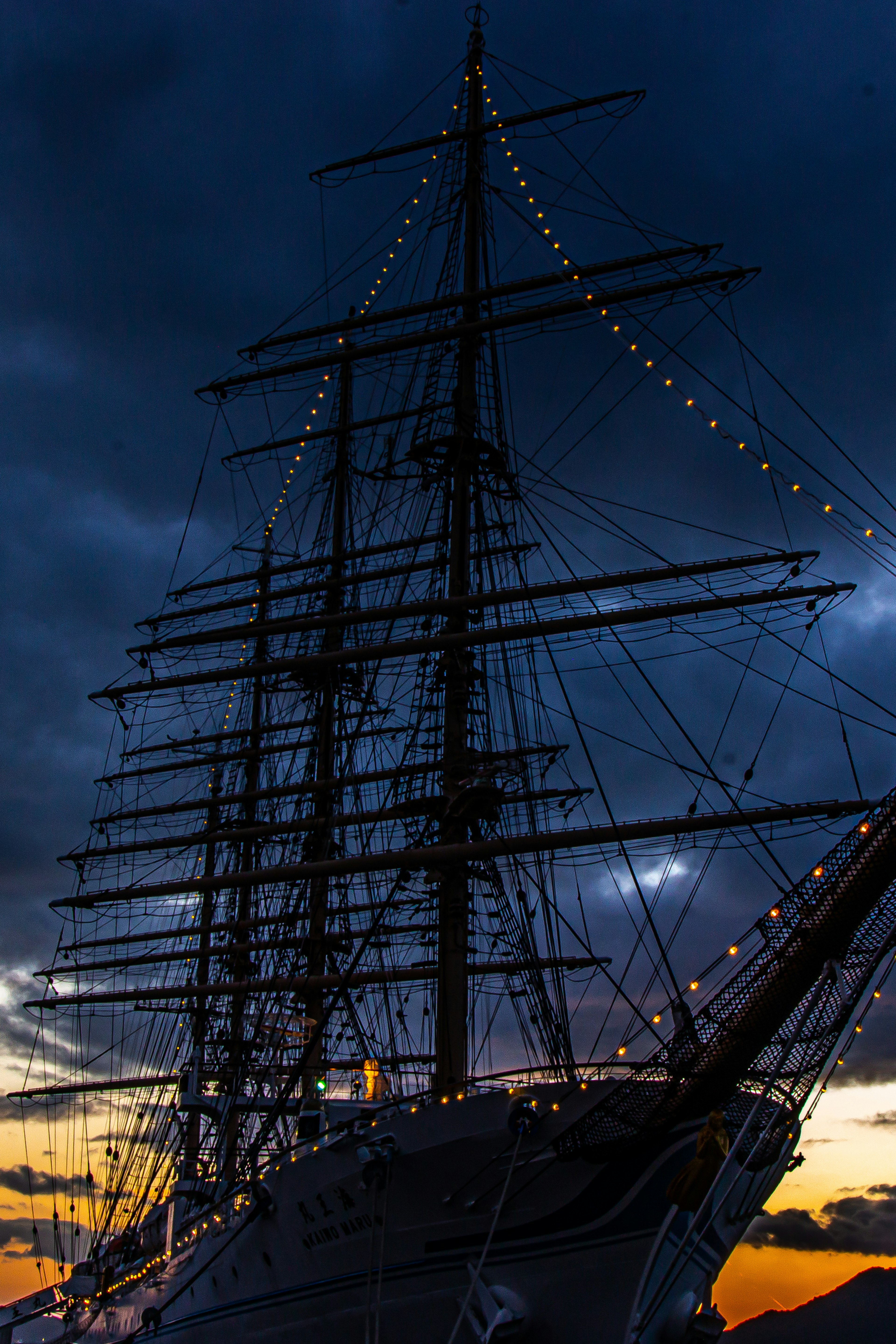 Silhouette of a sailing ship with illuminated masts against a sunset sky