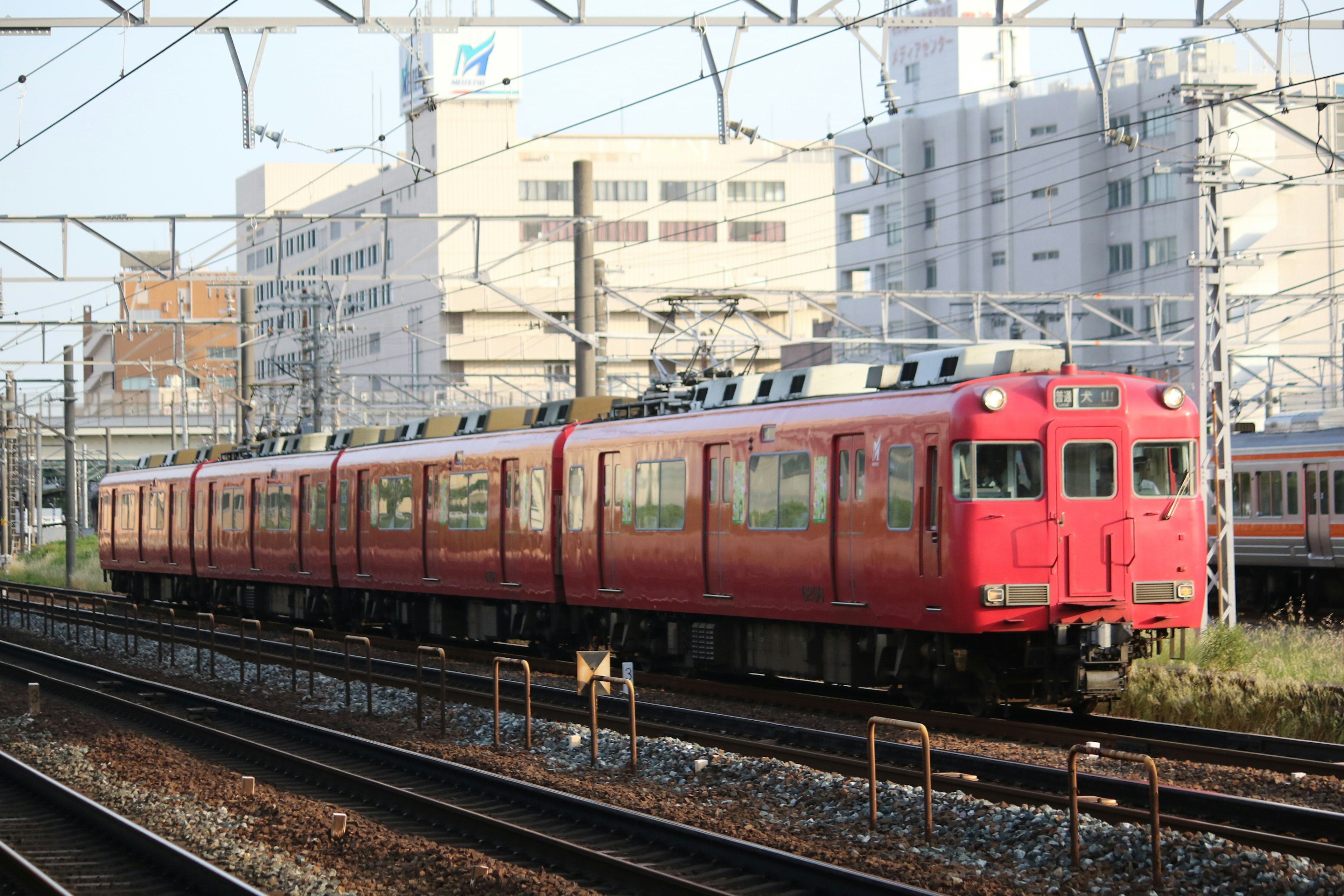 รถไฟสีแดงวิ่งบนรางรถไฟมีอาคารอยู่ด้านหลัง