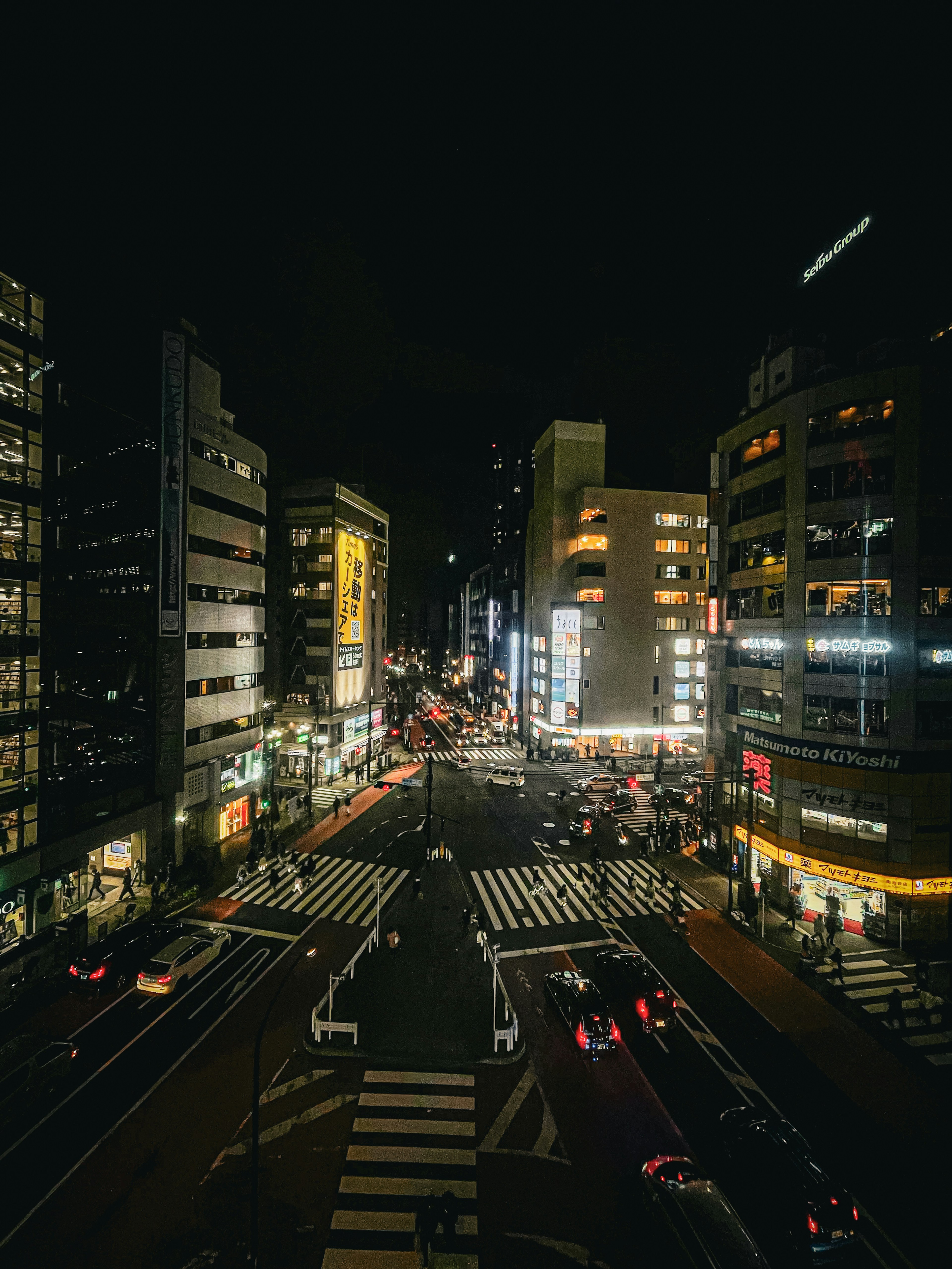 Paisaje urbano nocturno con edificios altos y una intersección concurrida iluminada por luces de coches