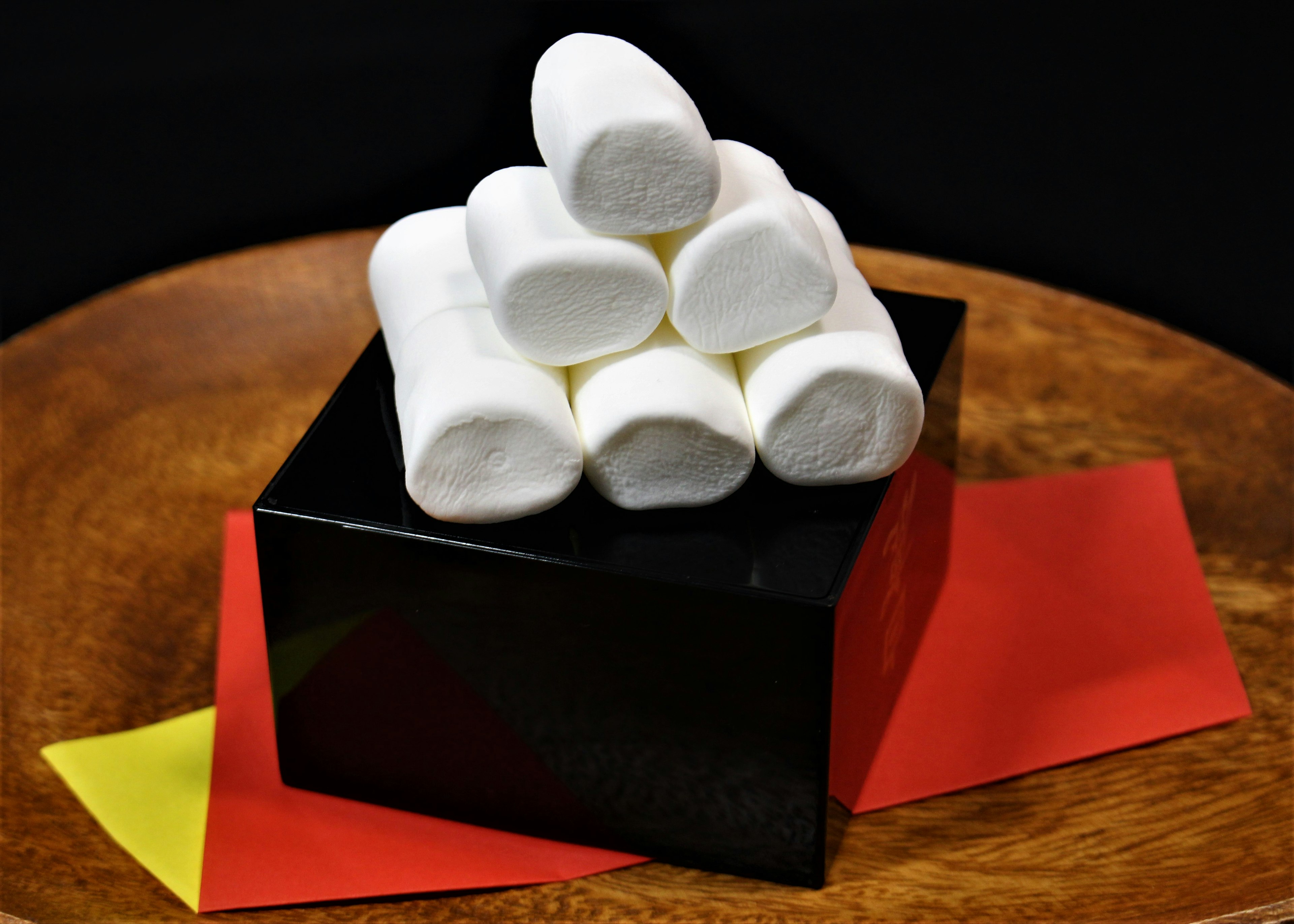 Kim tự tháp marshmallow trắng trên hộp đen với giấy đỏ và vàng bên dưới