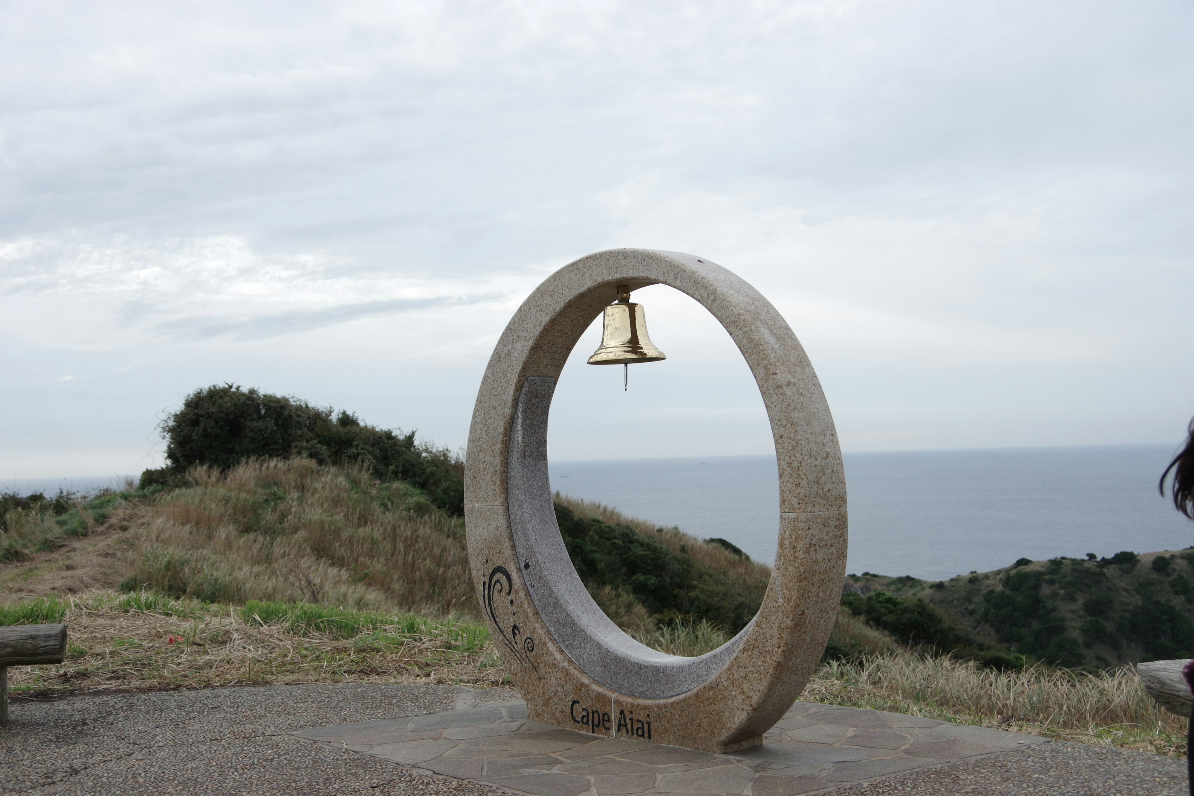 Monumento circular de piedra con una campana con vista al mar