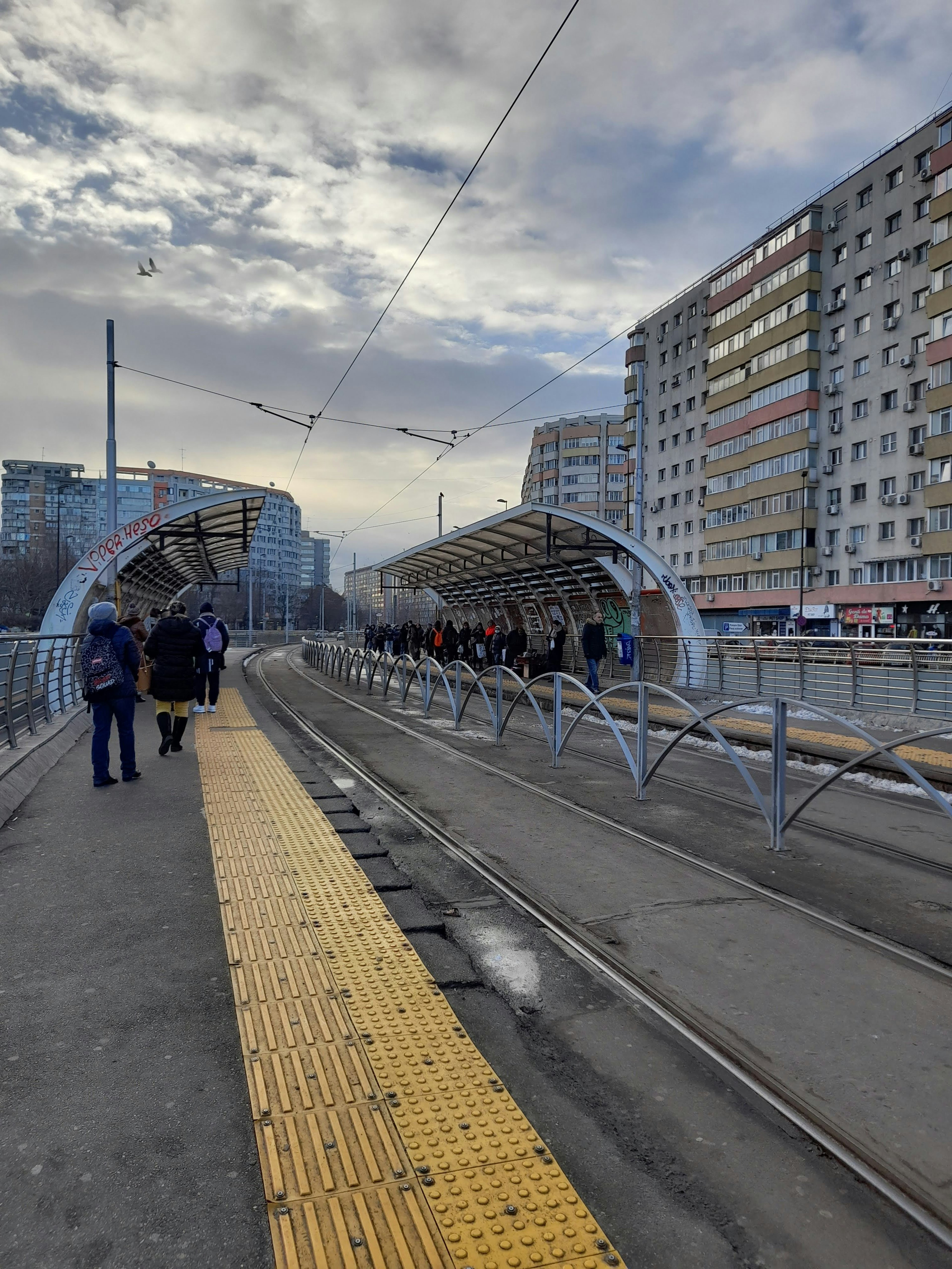 Urban tram stop scene with people waiting buildings in the background