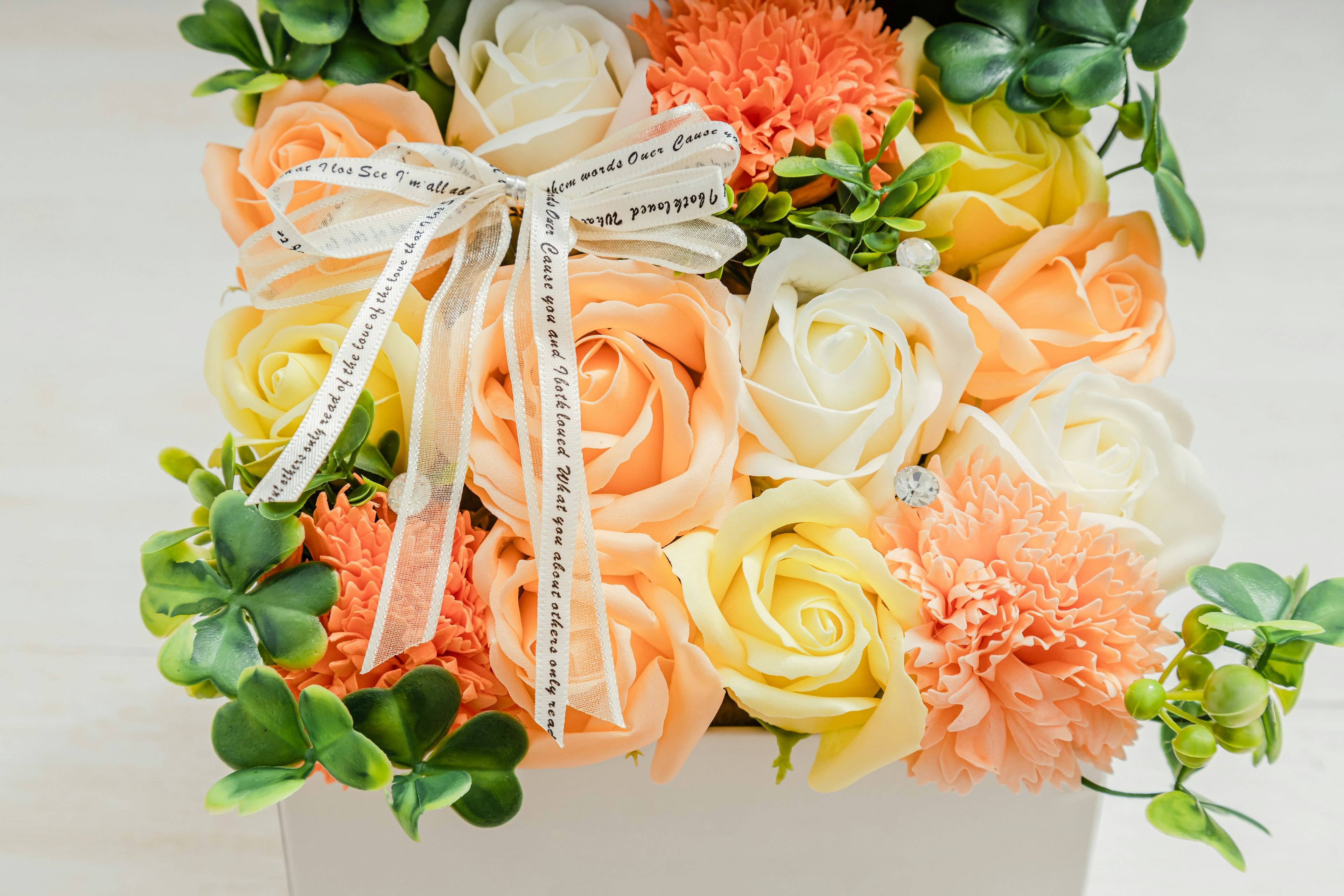 Ein Blumenarrangement mit Pfirsich- und weißen Rosen sowie orangefarbenen Nelken, die mit einem Band gebunden sind