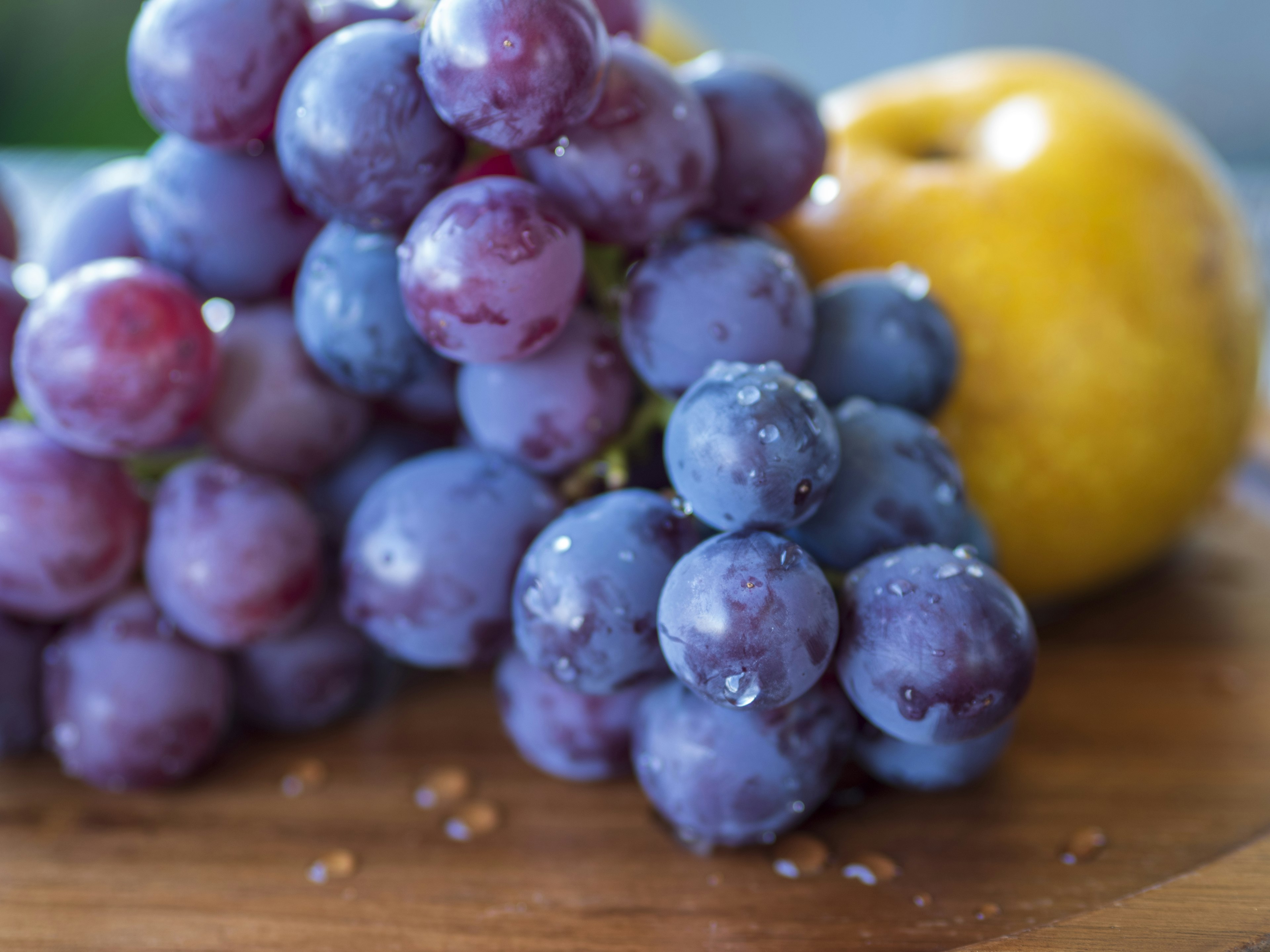 Uvas moradas y una manzana amarilla dispuestas sobre una tabla de madera