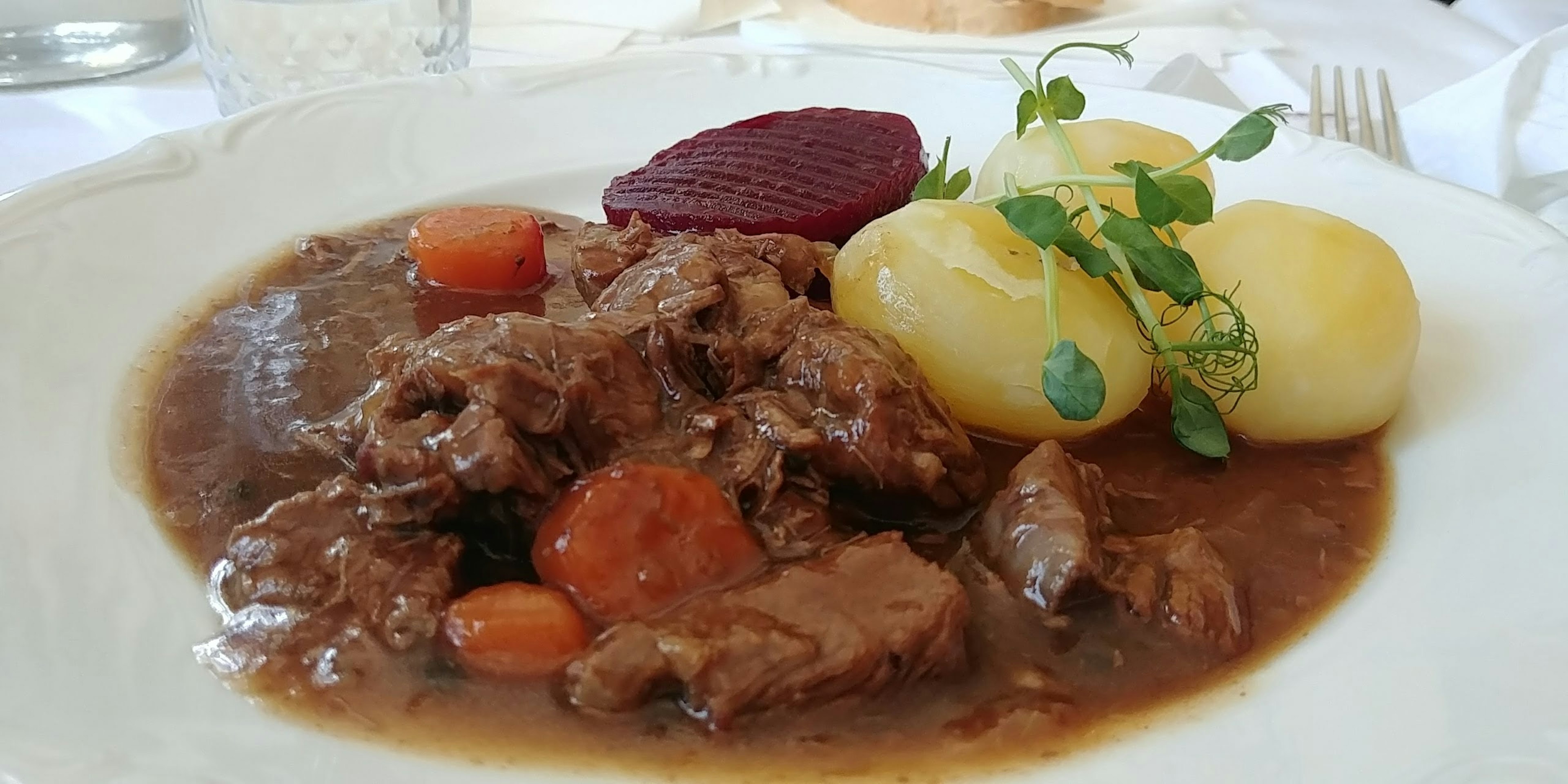 Un piatto di stufato di carne con carote e patate guarnito con erbe