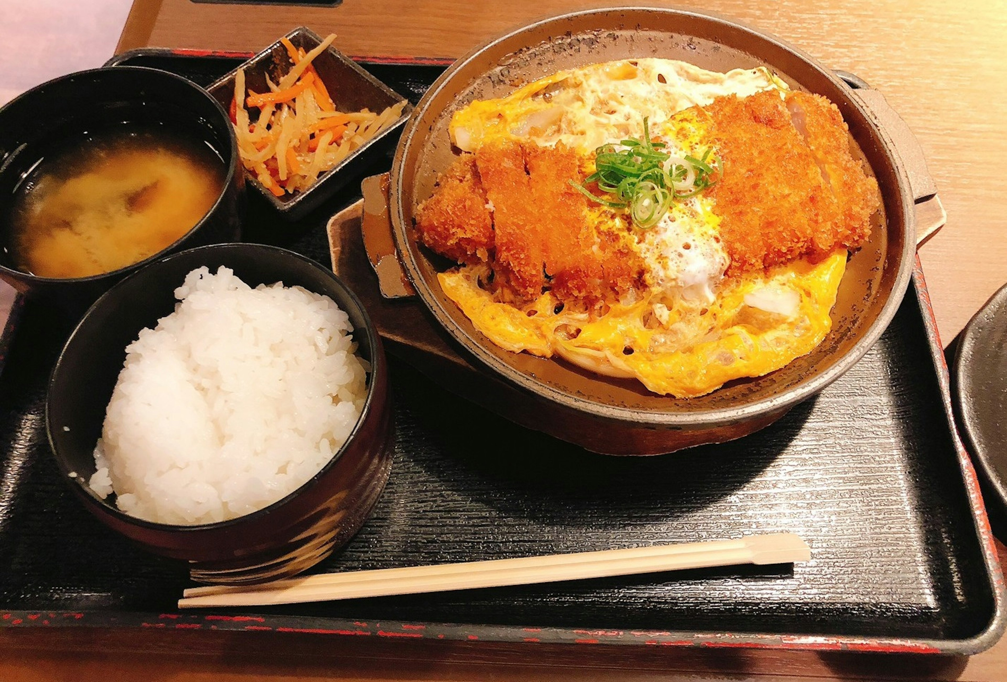 A bowl of katsudon with rice and miso soup served alongside shredded vegetables