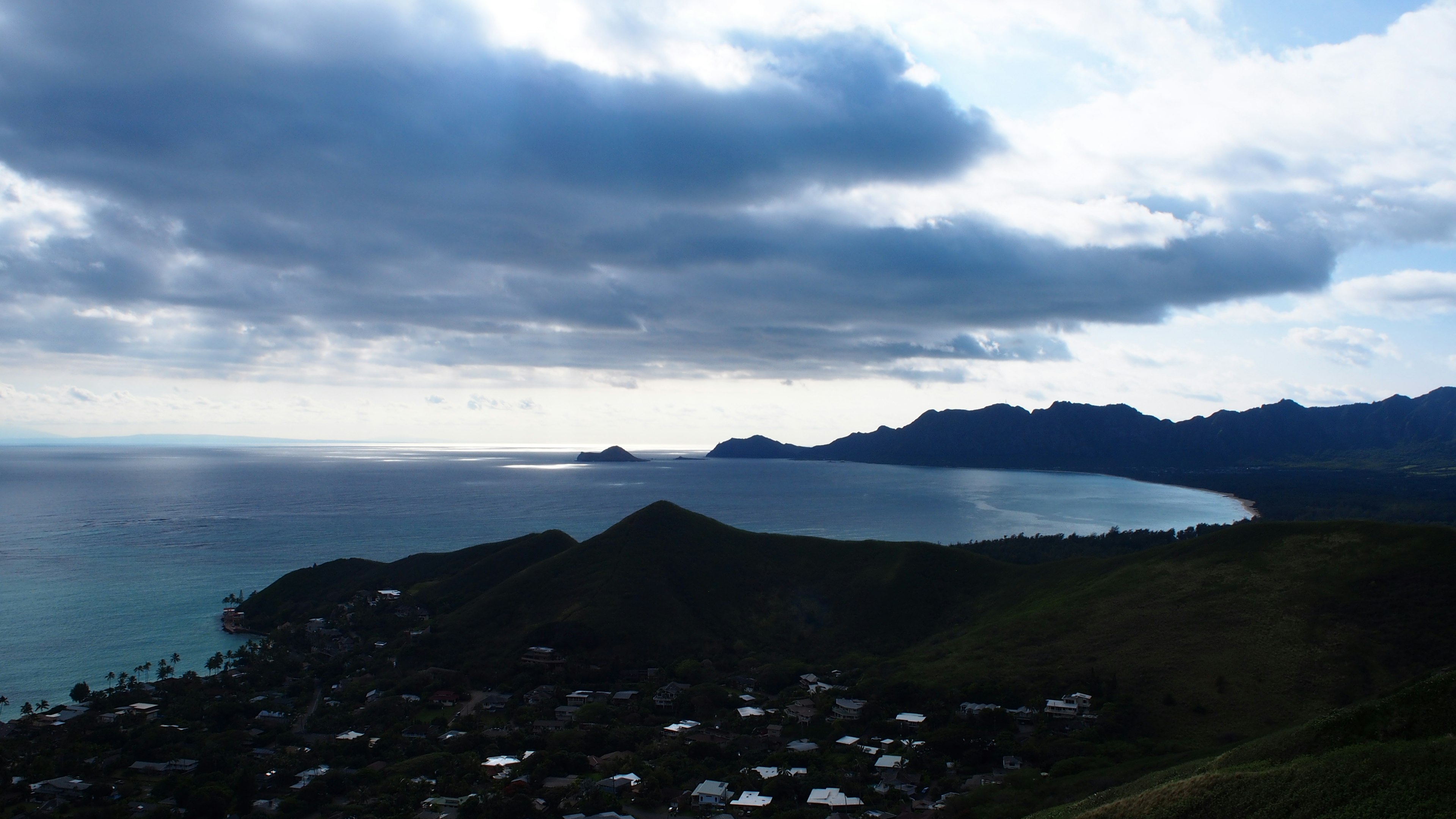 Scenic view of ocean and mountains with expansive clouds above