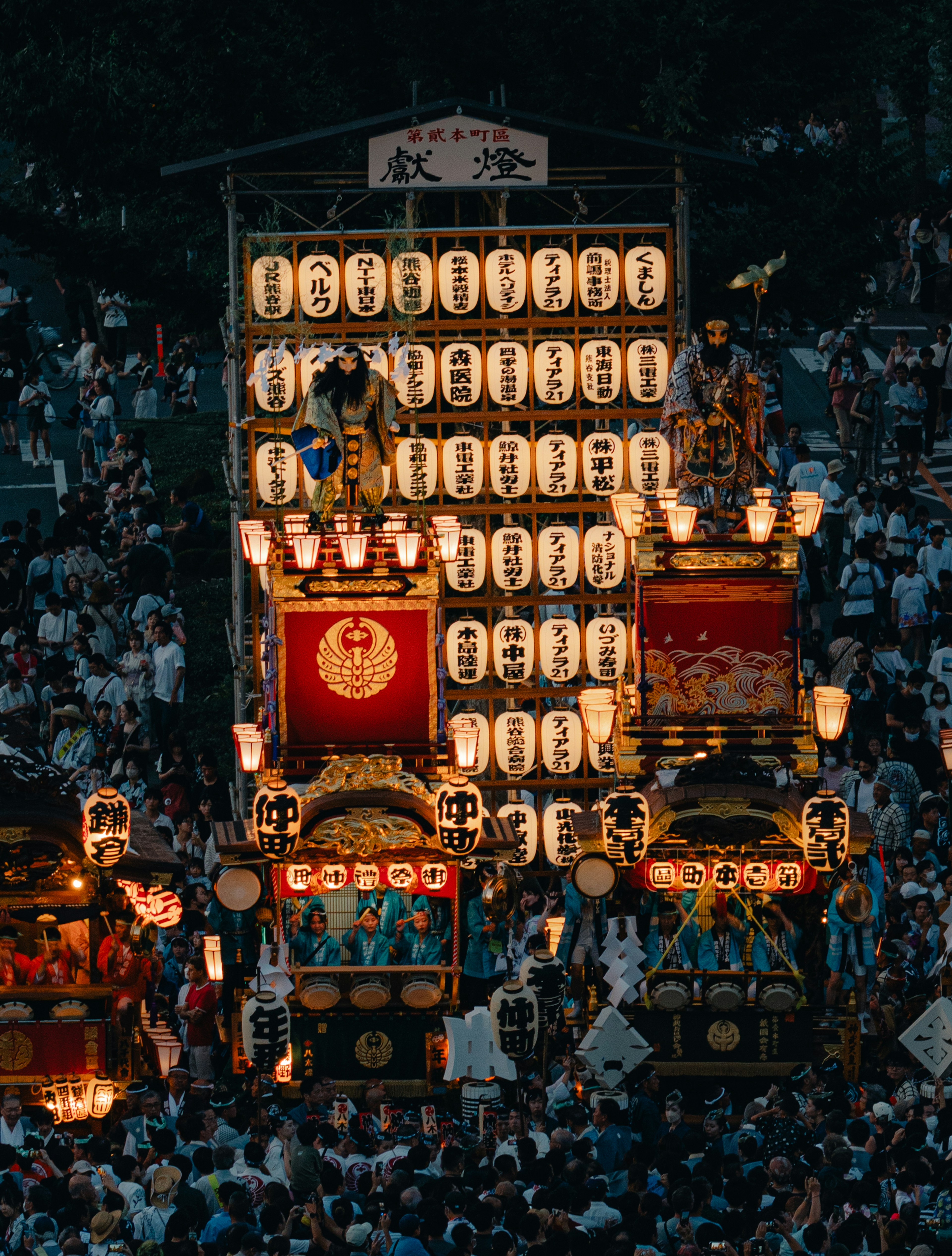 Une scène de festival vibrante avec des lanternes illuminées et des chars la nuit