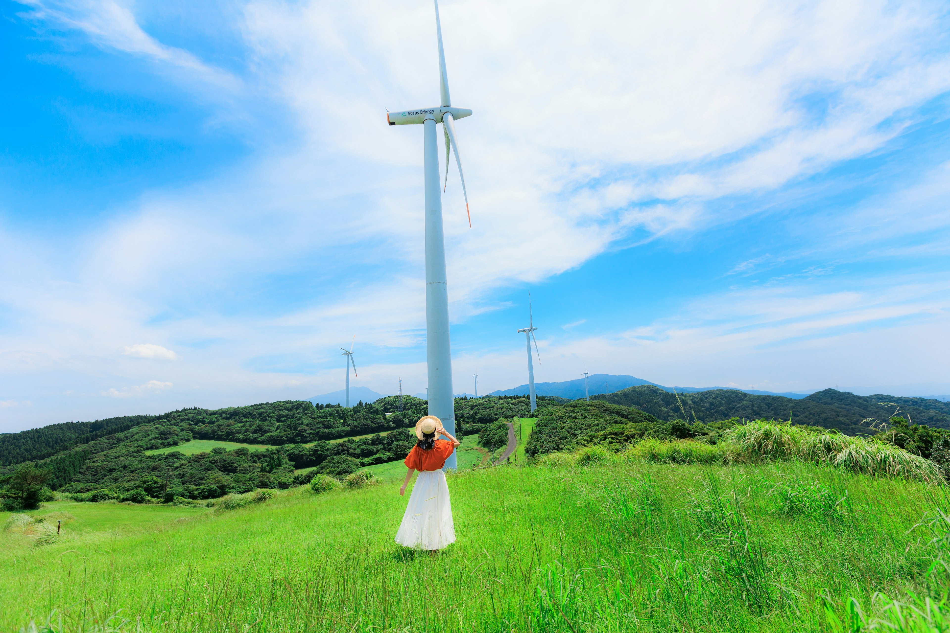 Woman standing near wind turbine with blue sky and green hills