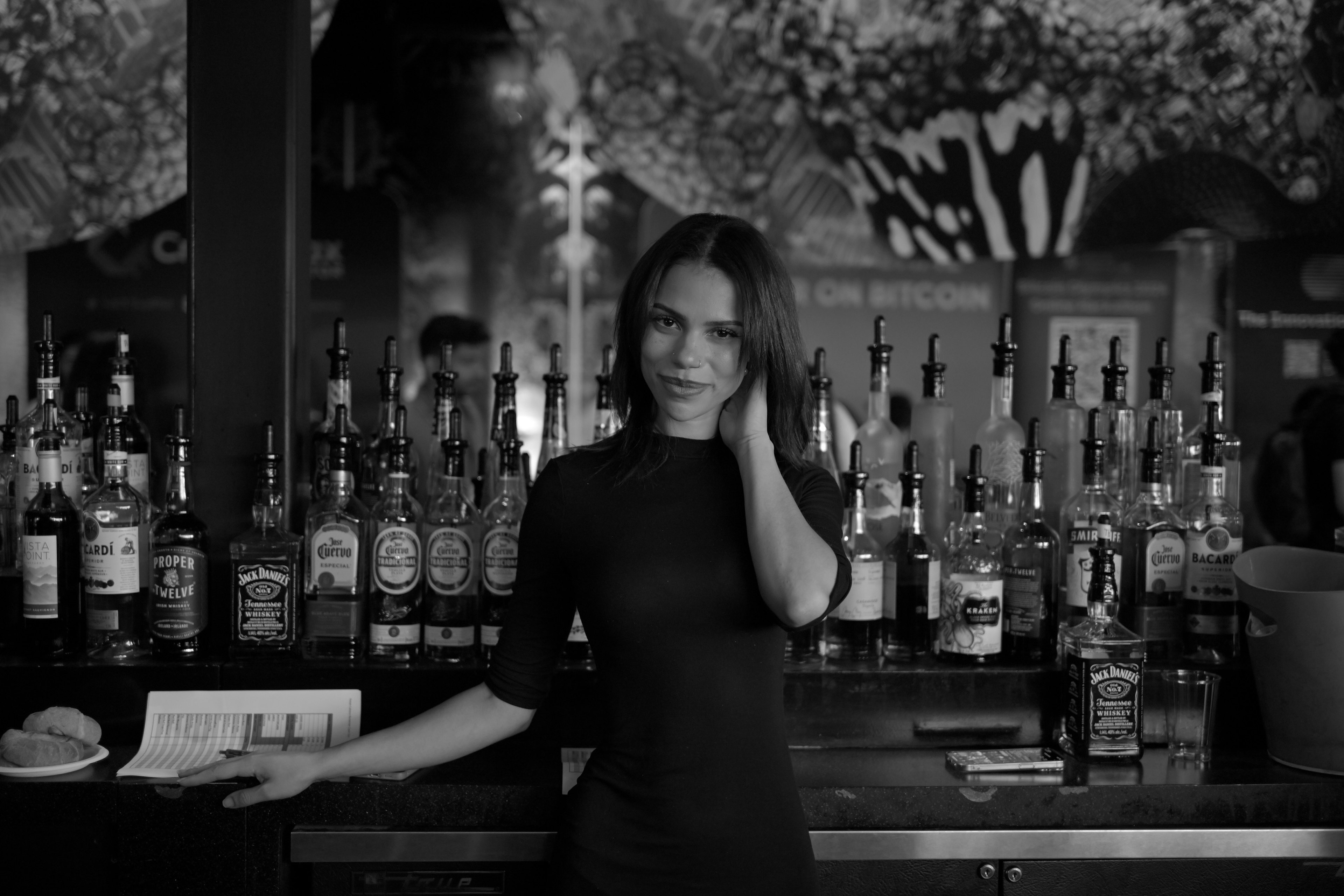 Mujer bartender de pie frente a un bar con varias botellas