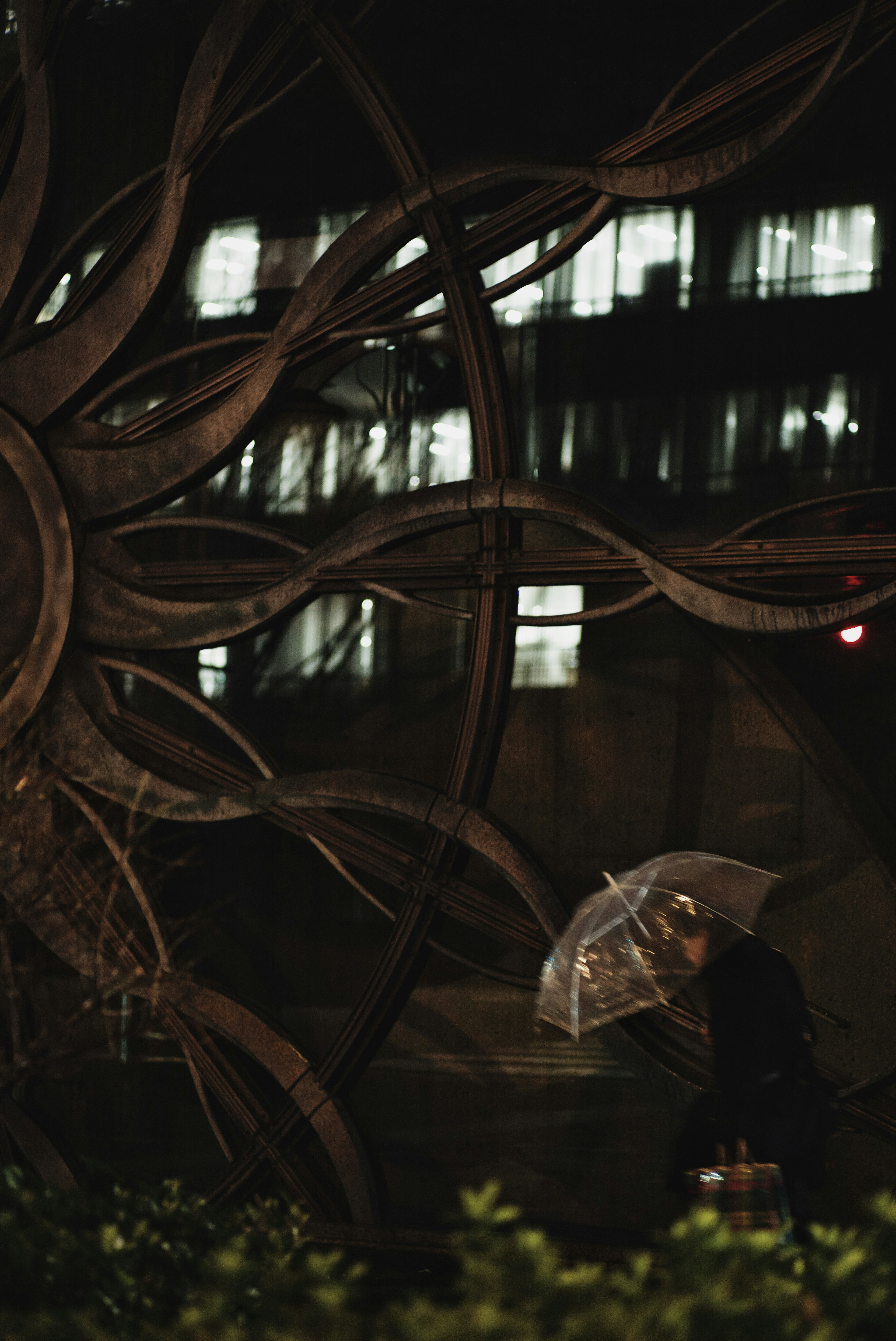 Une personne tenant un parapluie transparent marchant devant une grande sculpture la nuit