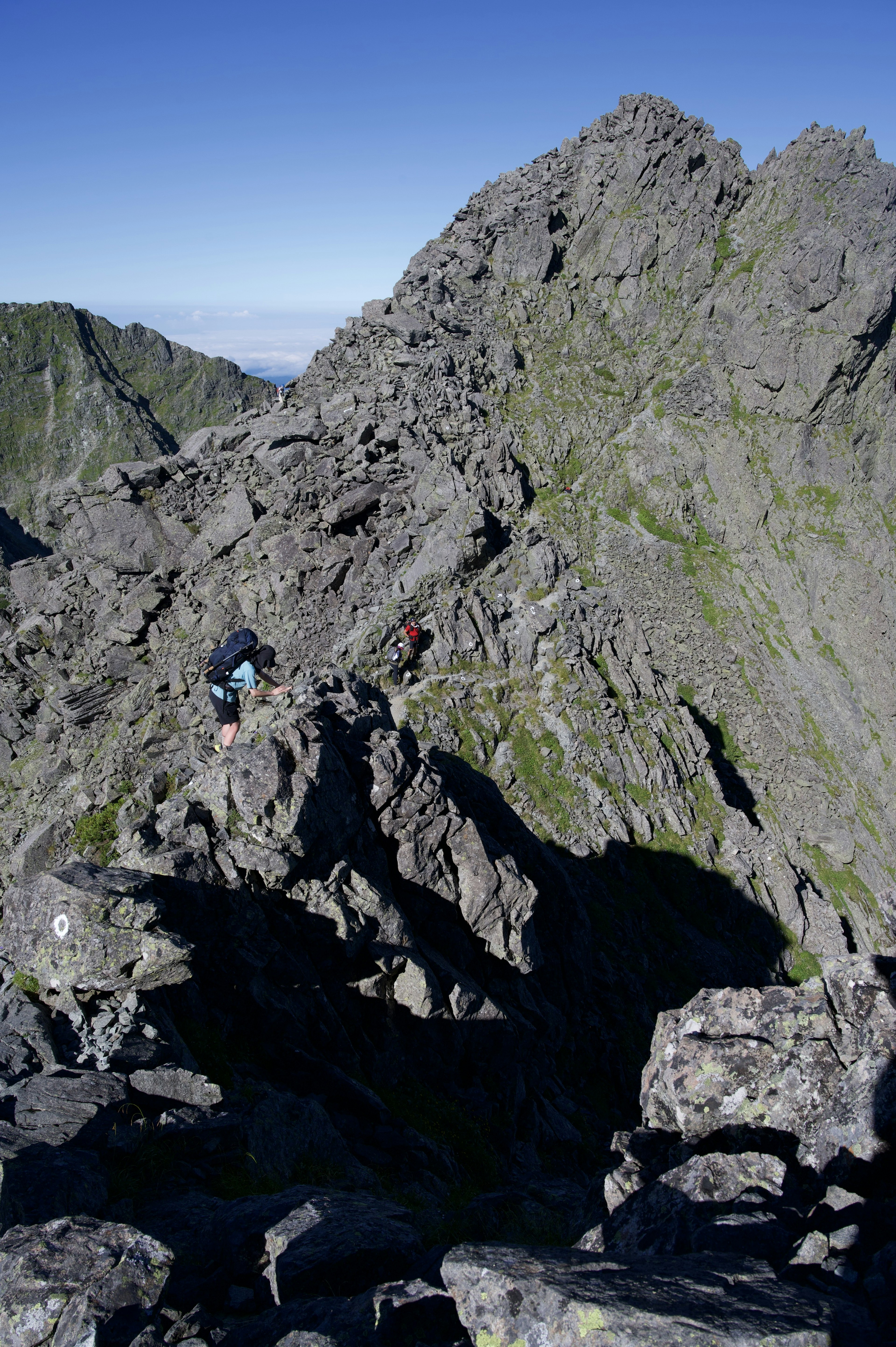 険しい山の岩場を登る登山者たち青空と緑の山々が背景にある