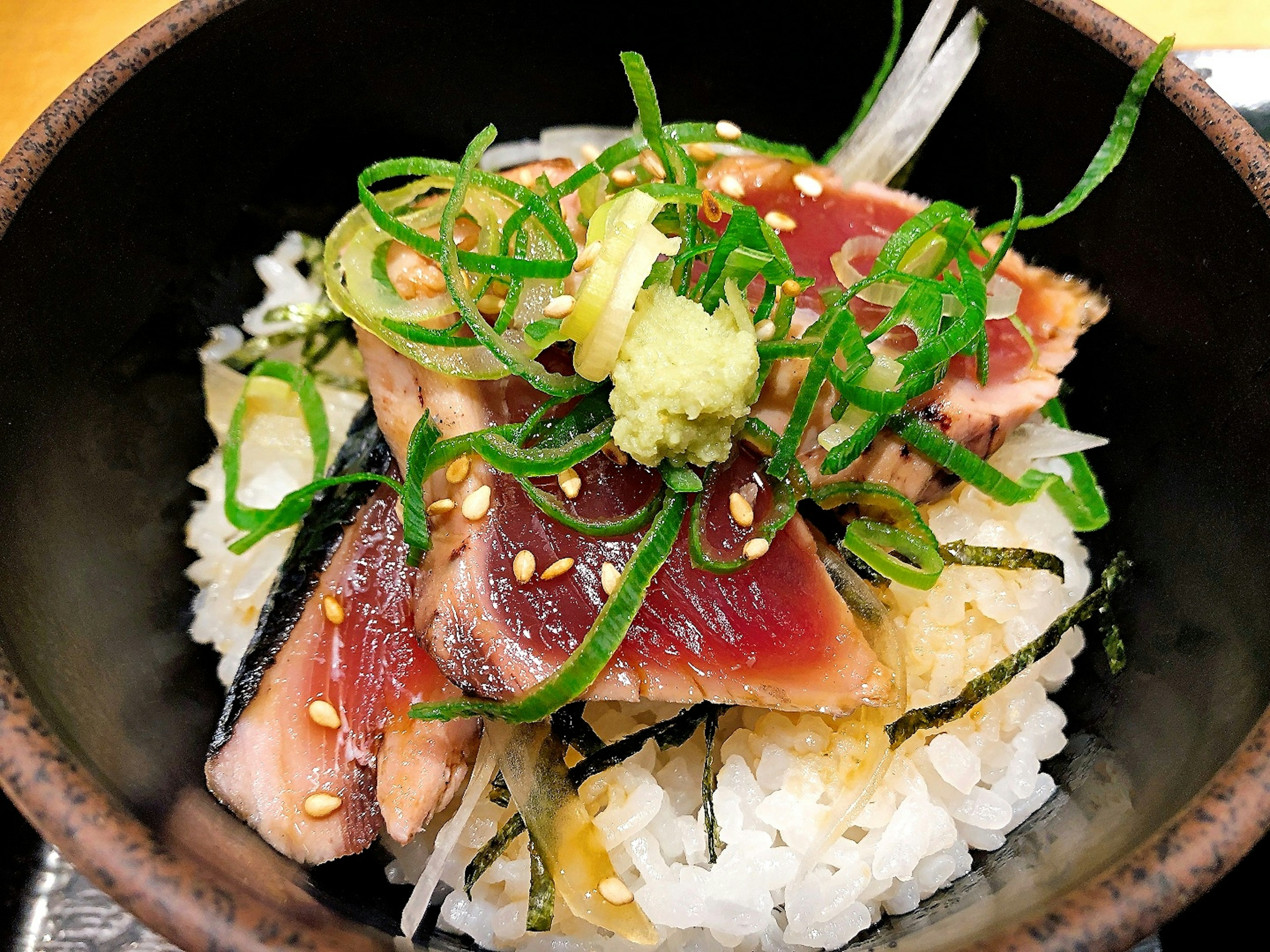 まぐろの刺身とご飯の丼にネギとわさびがトッピングされている