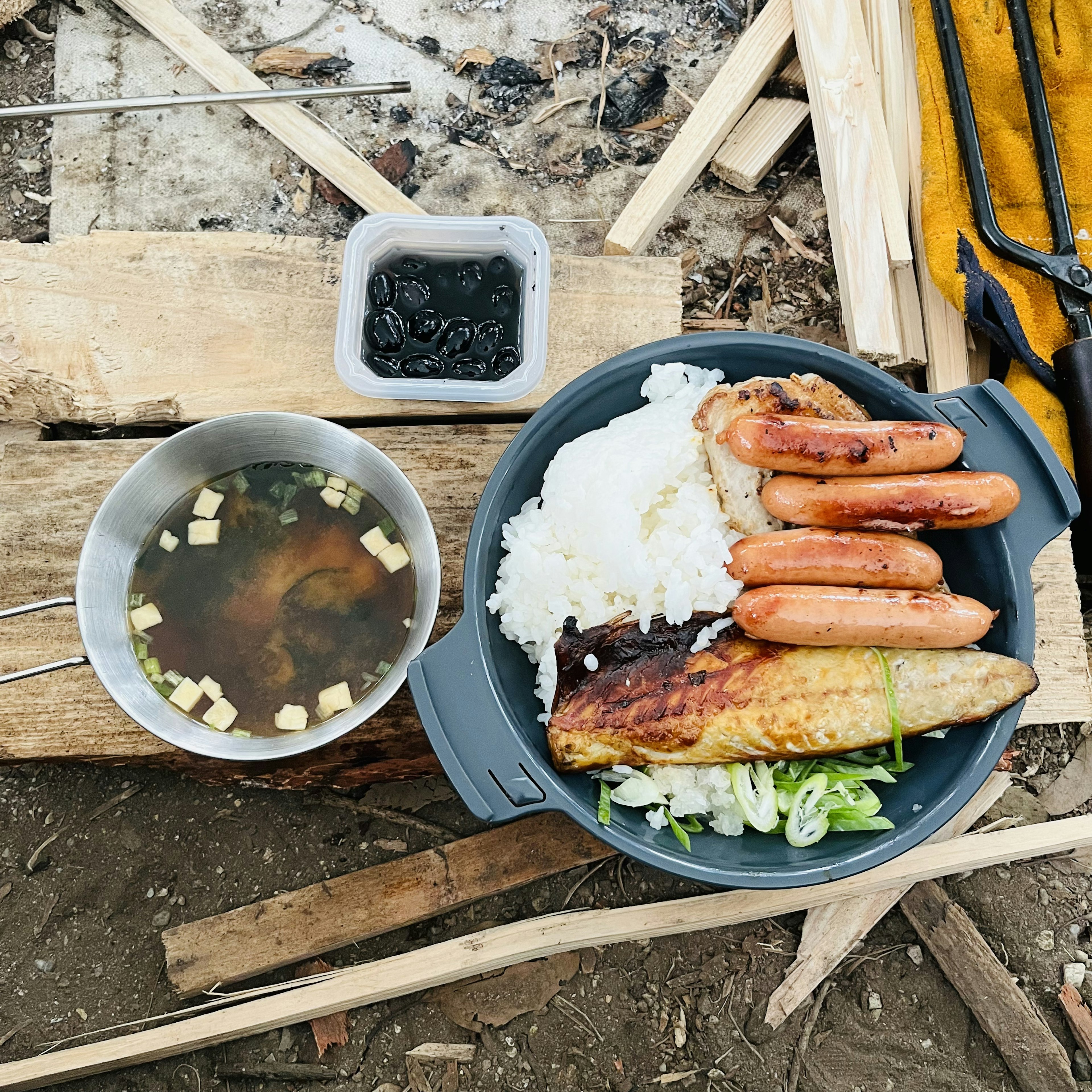 キャンプ料理の皿に盛られた白ご飯とグリルした魚、ソーセージ、スープ