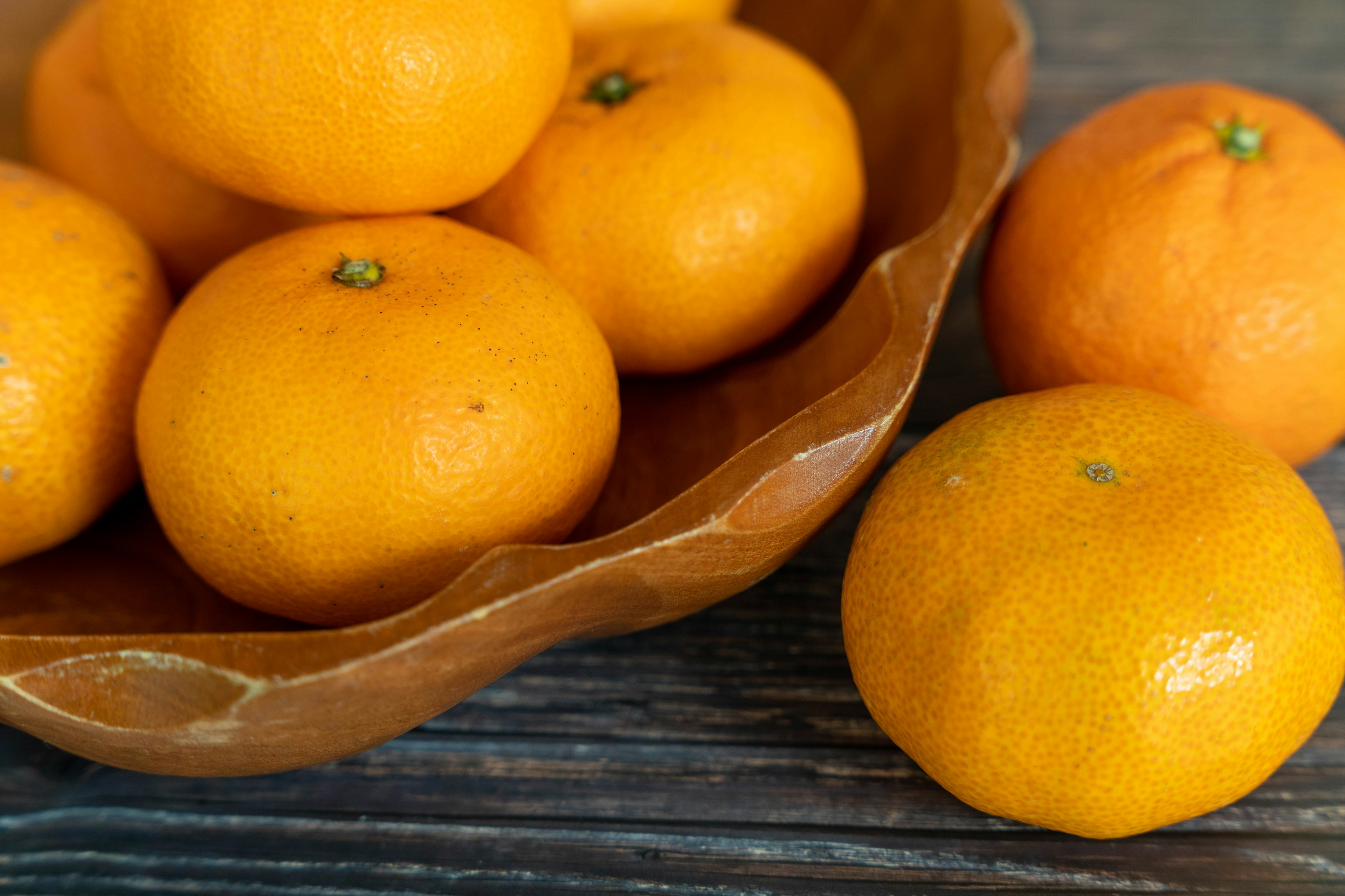 Mangkuk kayu penuh dengan jeruk mandarin oranye cerah di atas permukaan kayu