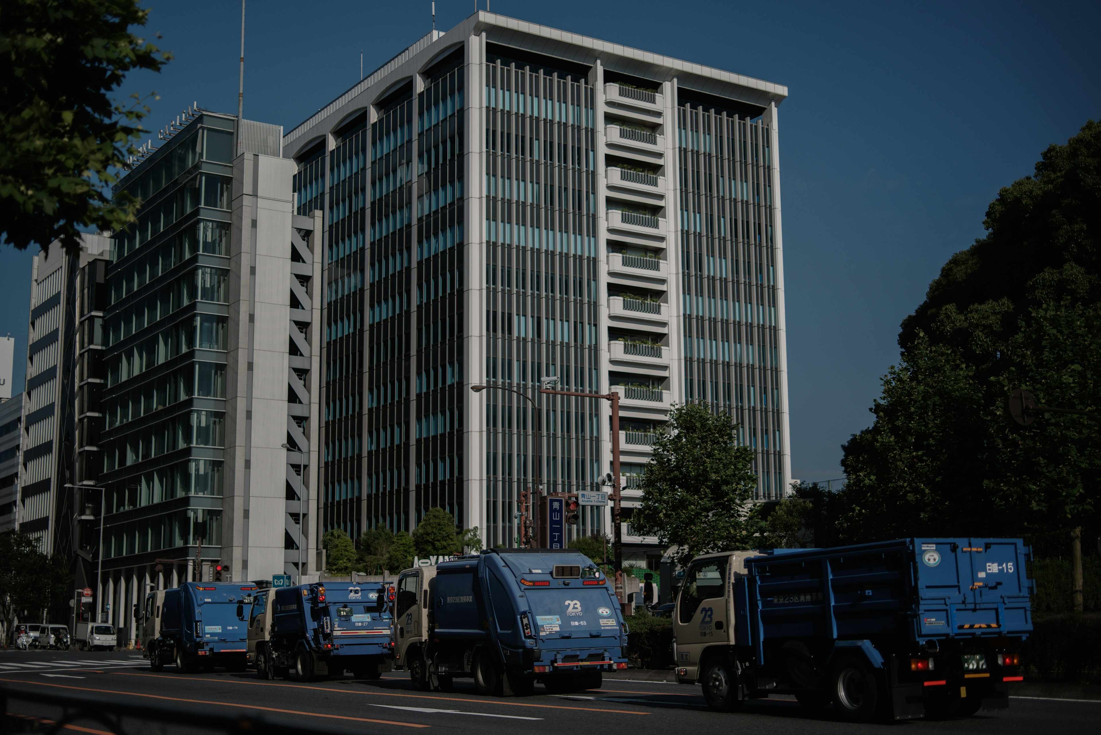 Fila de camiones de basura azules frente a un edificio moderno