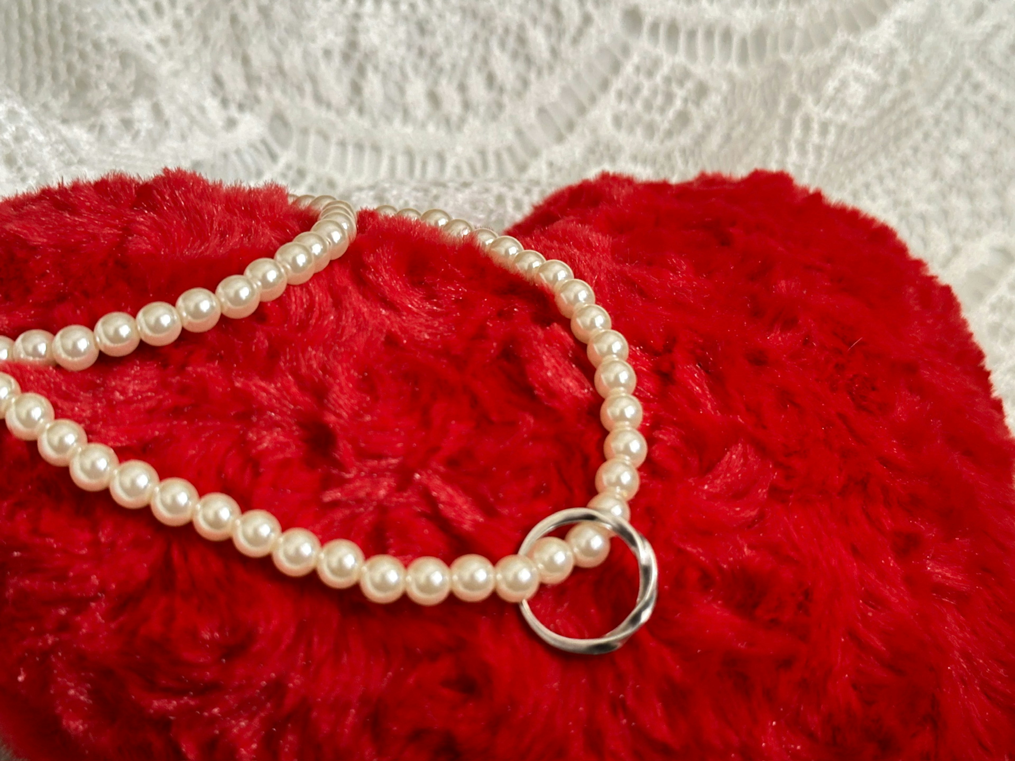 Pearl necklace with a silver ring resting on a red heart