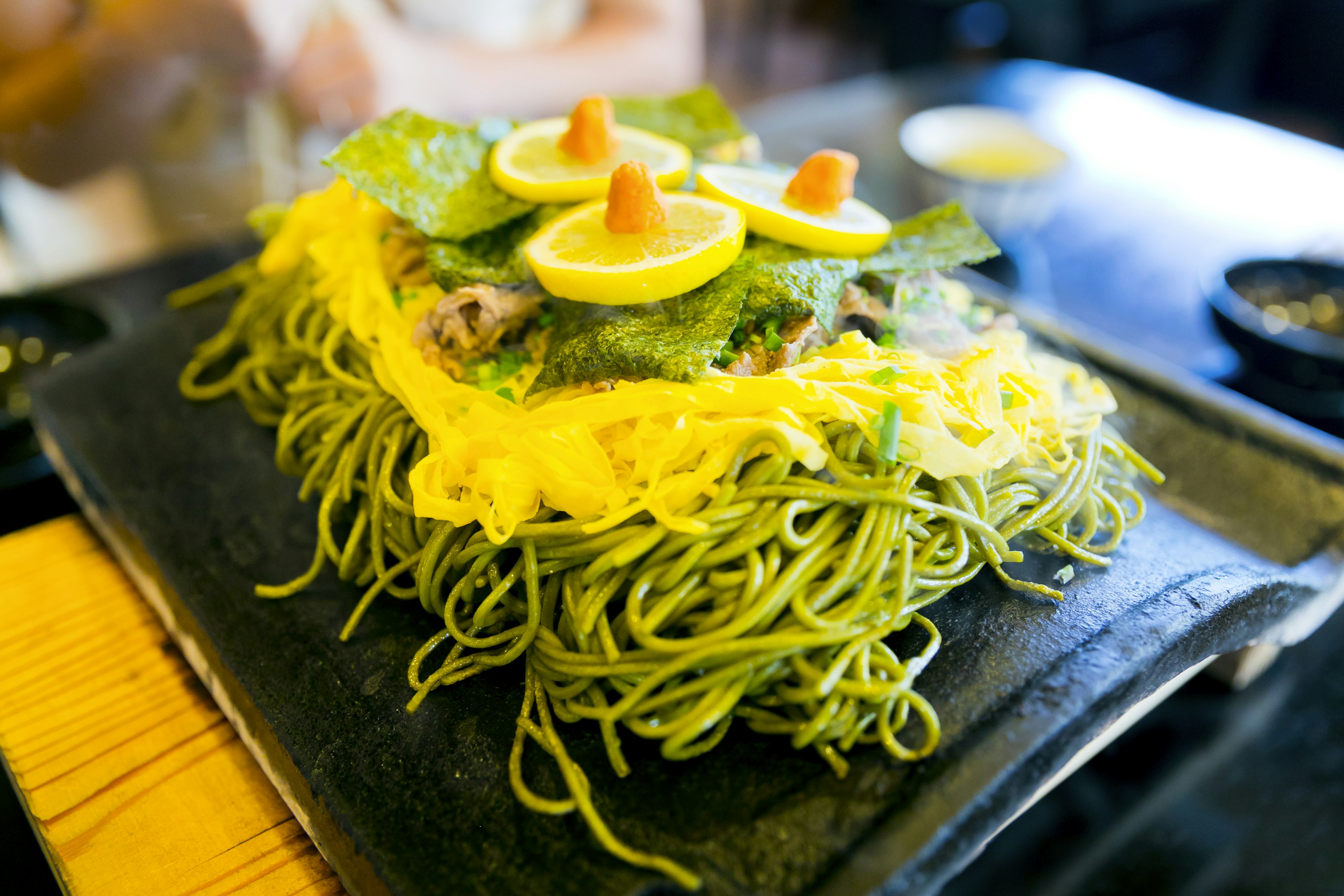 Piatto con noodles verdi guarniti con lattuga, fette di limone e uova di pesce