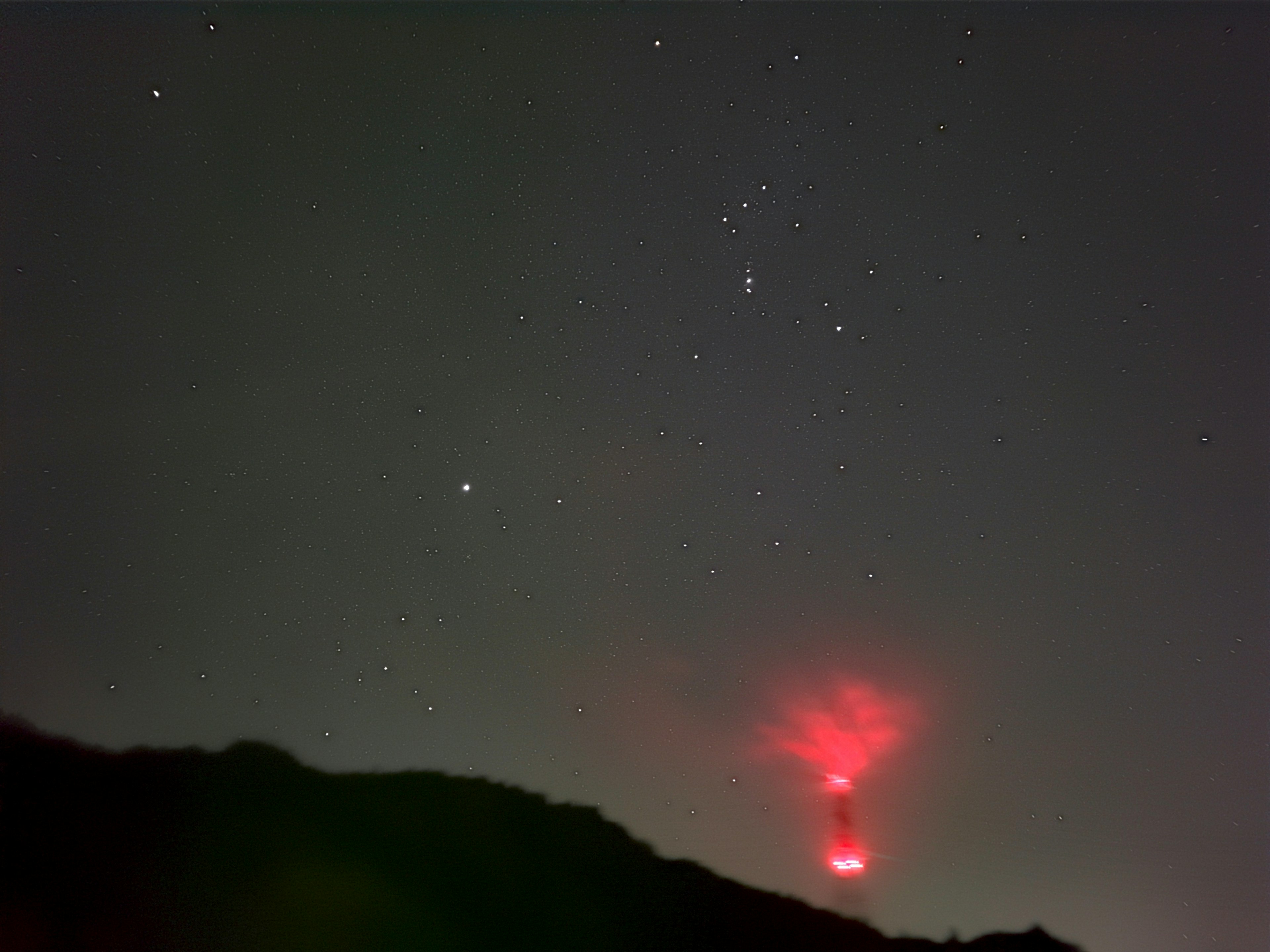 夜空に浮かぶ星々と赤い光を発する山のシルエット