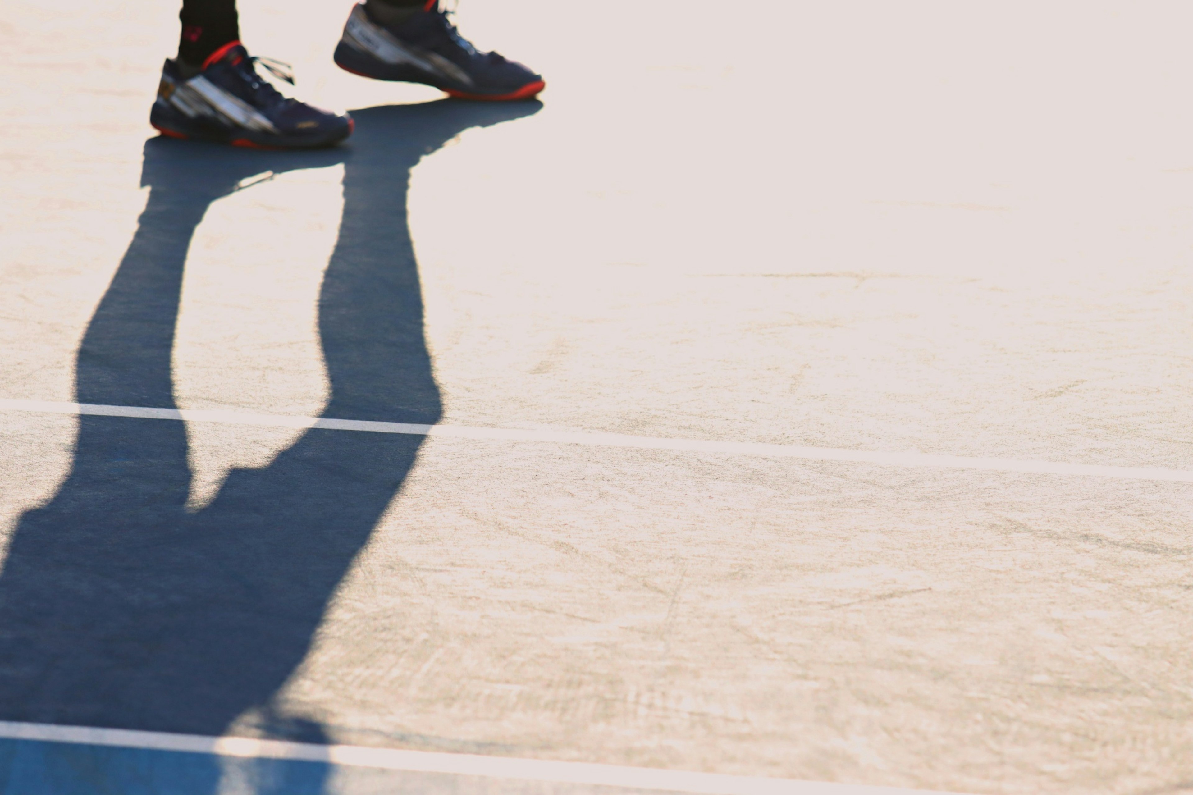 Close-up sepatu olahraga hitam di lapangan tenis dengan bayangan