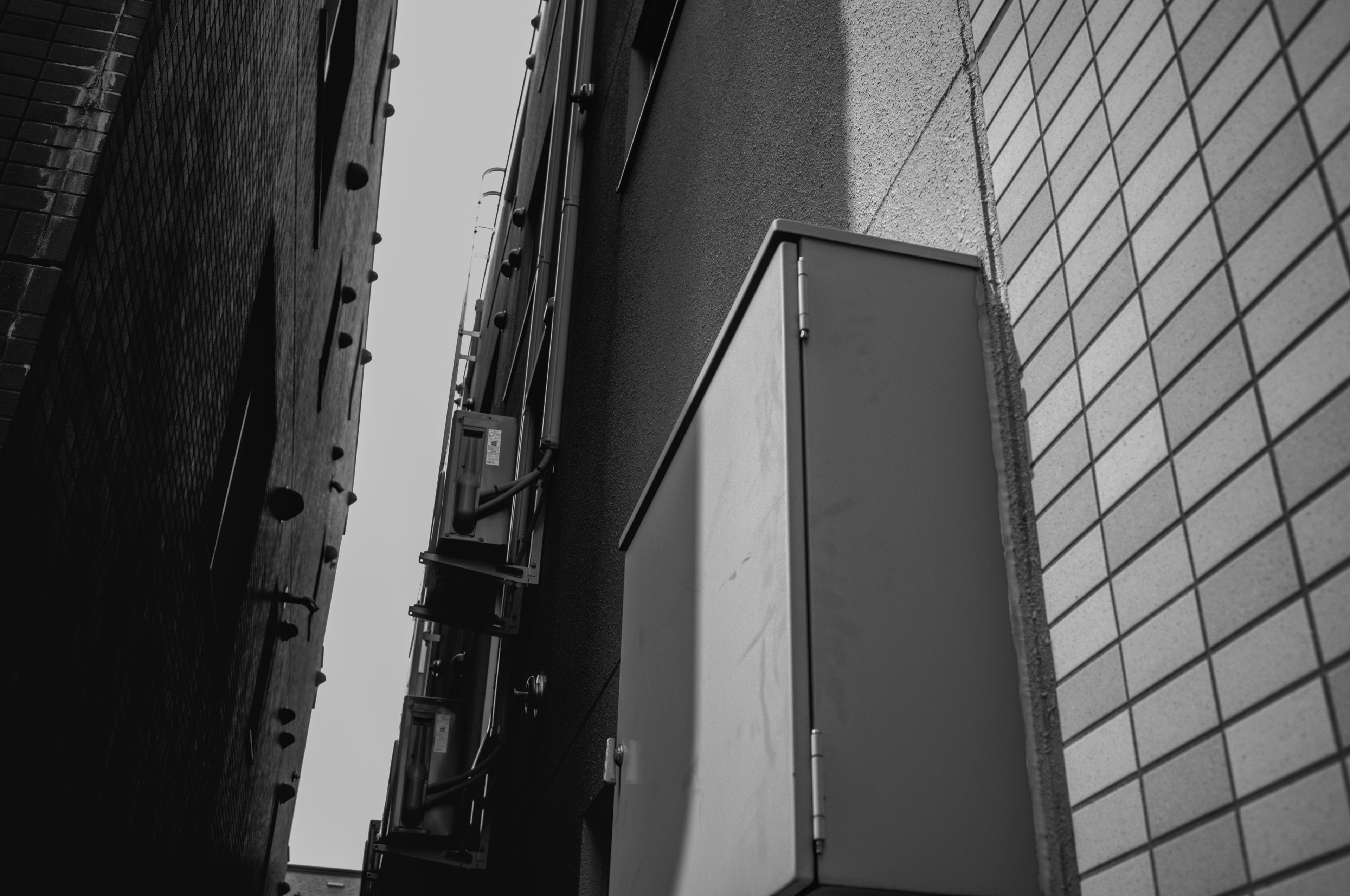 Narrow alley in black and white featuring tall walls and a box at the corner