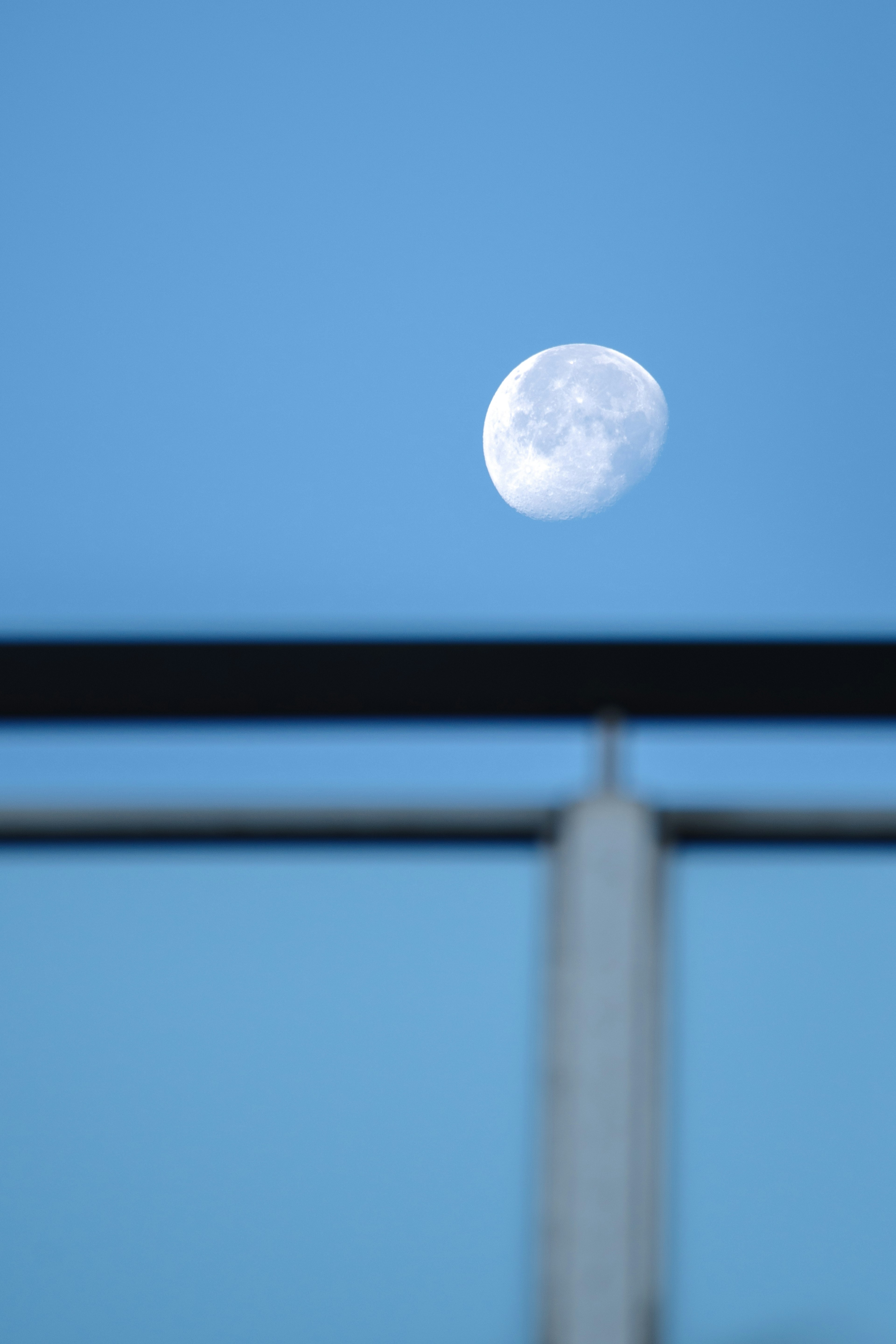 Primer plano de la luna en un cielo azul con una barandilla metálica