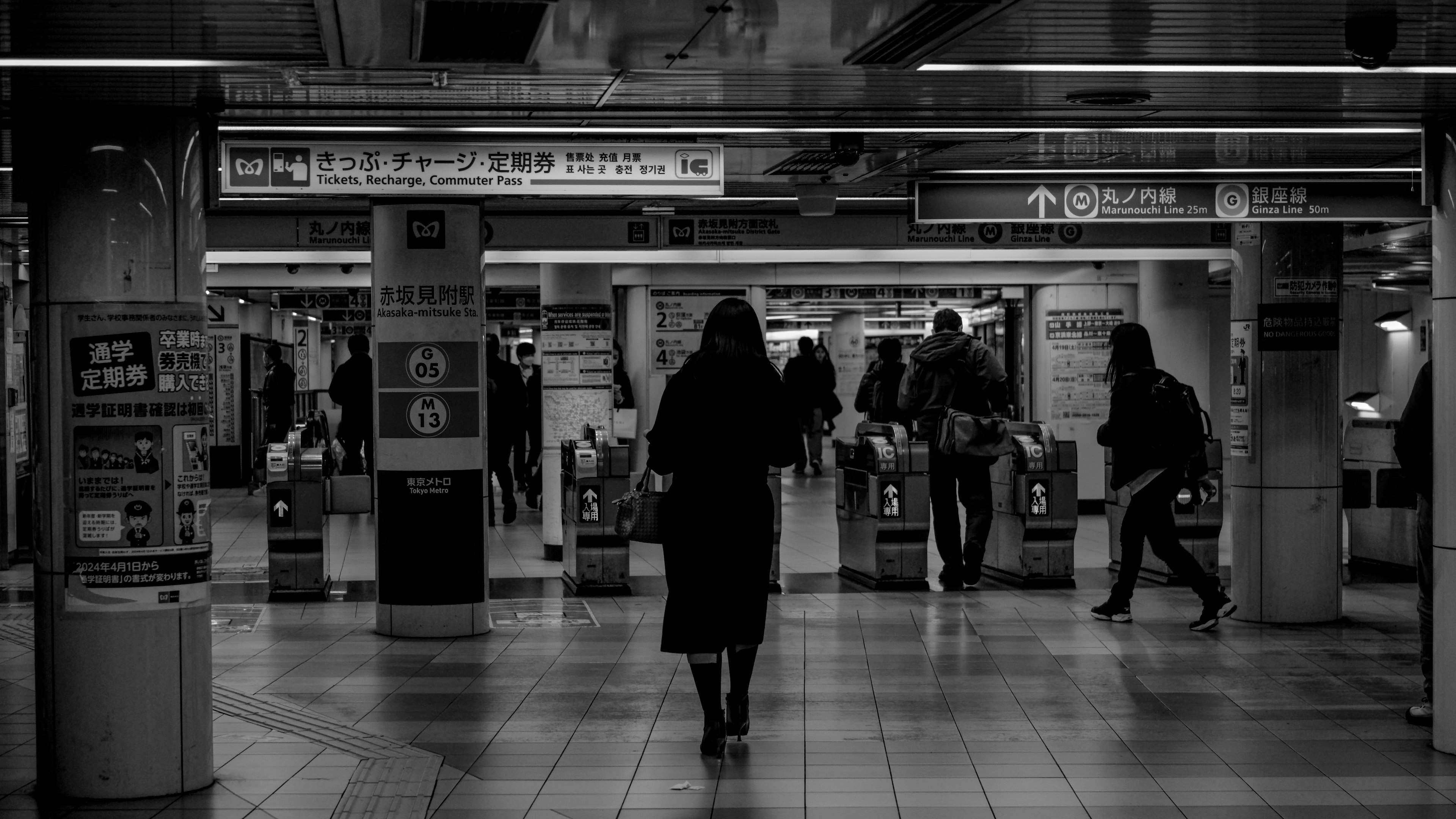 Scena di una stazione della metropolitana in bianco e nero con persone che camminano e una donna in primo piano