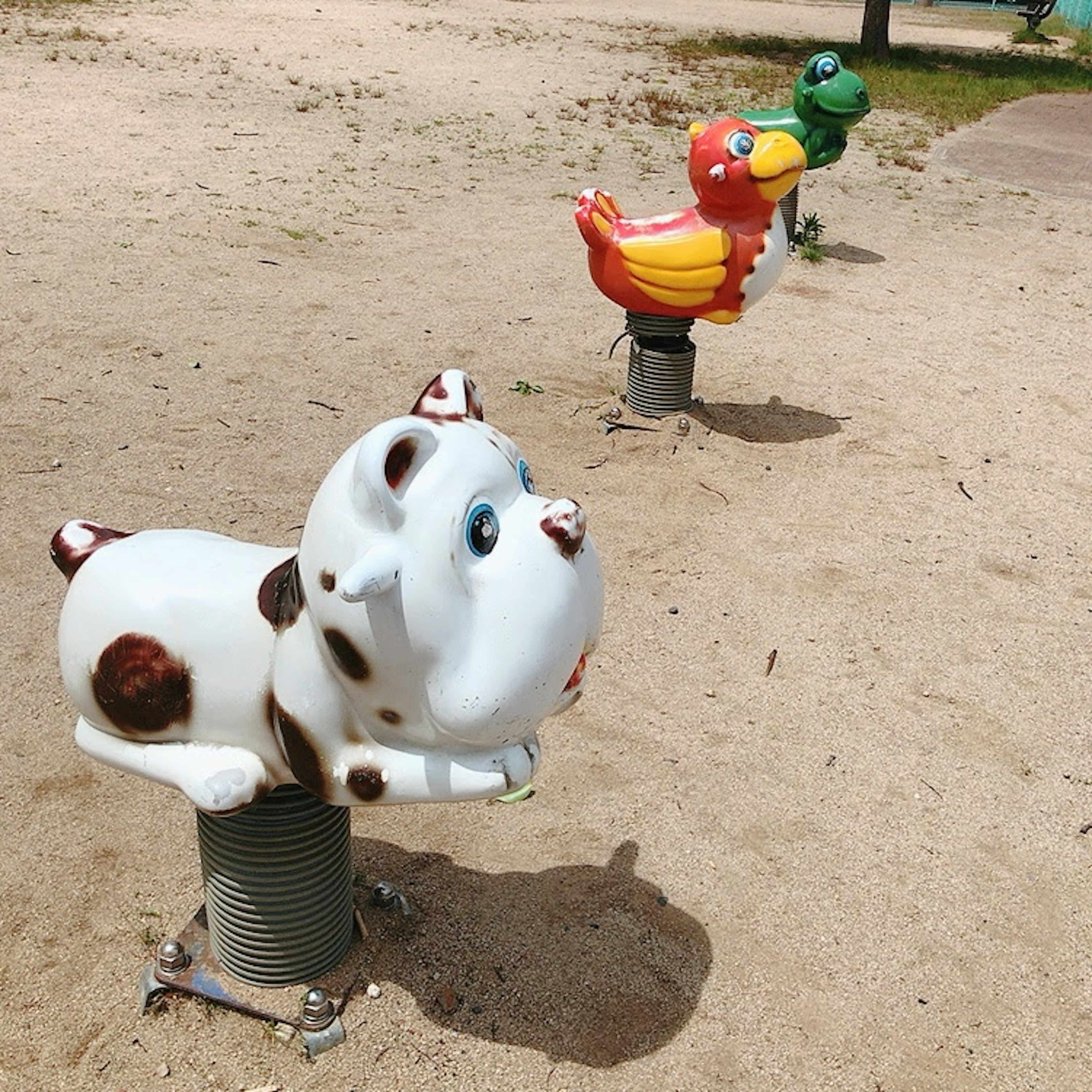 Federnde Spielgeräte in Tierform auf einem Spielplatz mit einem weißen Hund und einem bunten Vogel