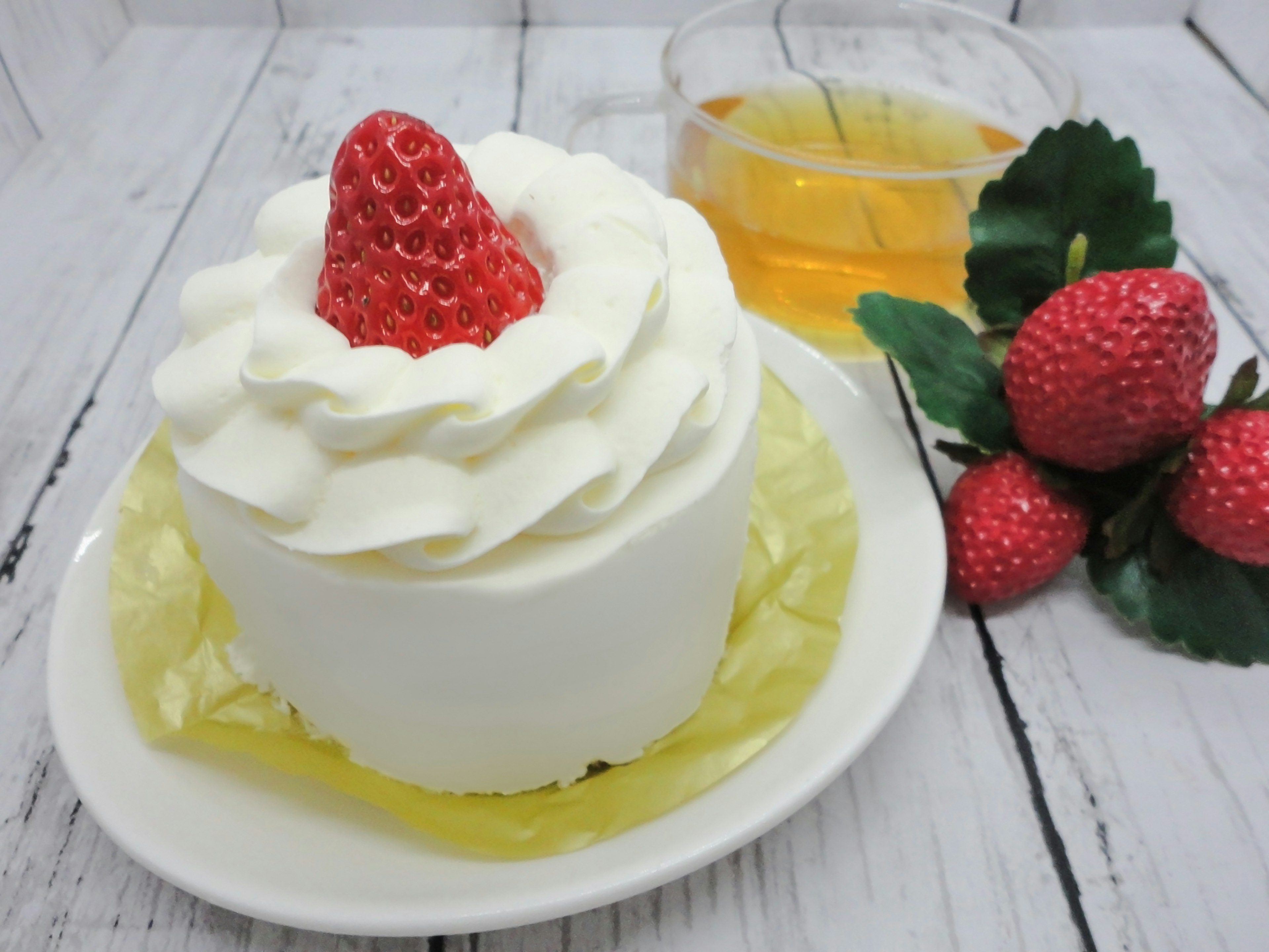 Image d'un gâteau garni de crème fouettée et d'une fraise à côté d'une tasse de thé