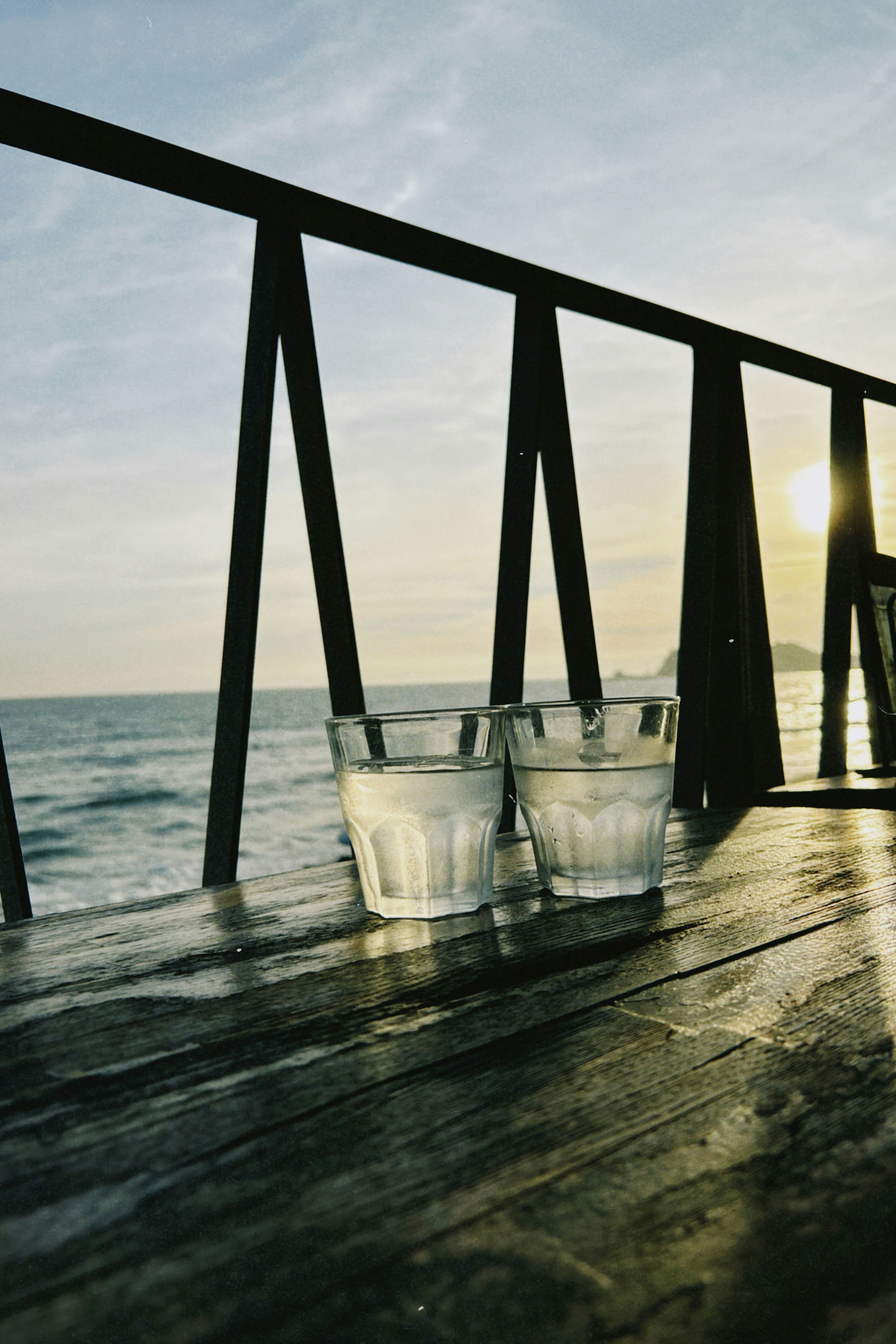 Two glasses of water on a wooden table with the ocean in the background