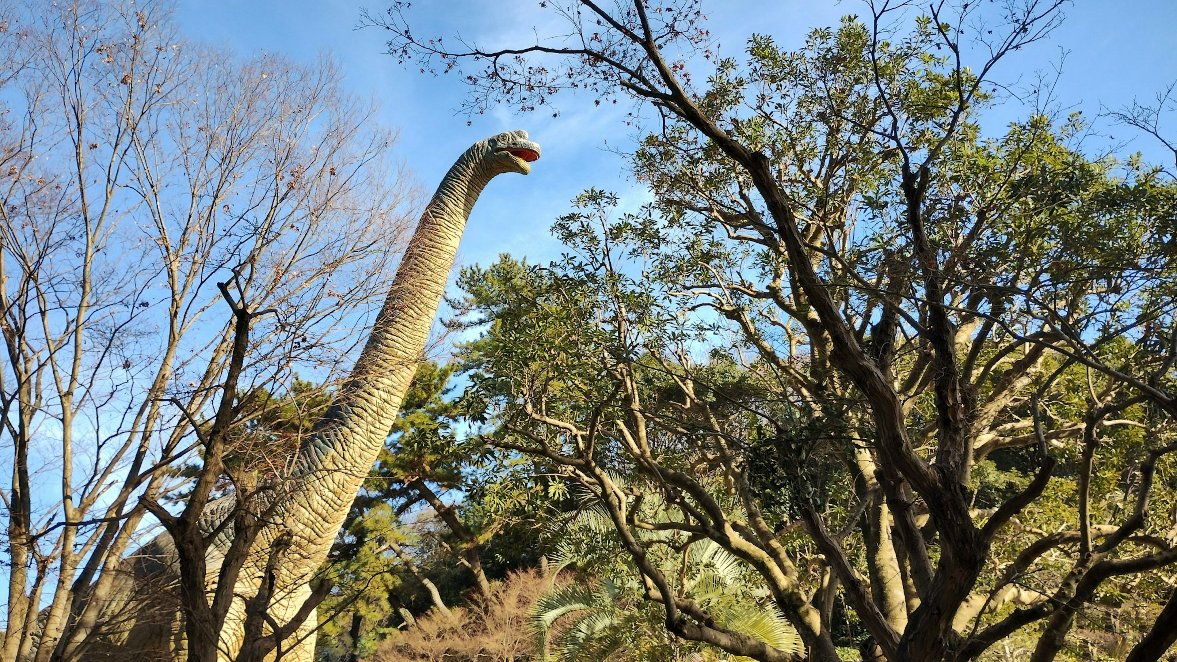 Large dinosaur model towering in a park surrounded by trees