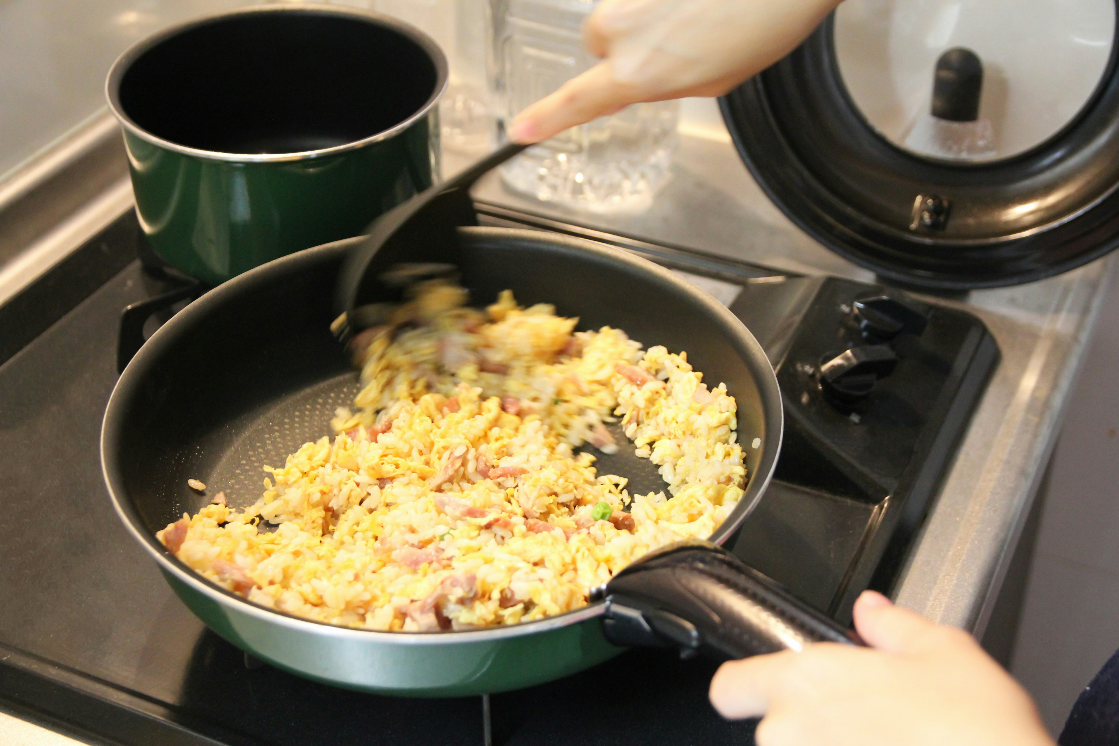 A frying pan with scrambled rice and ingredients being stirred by a hand