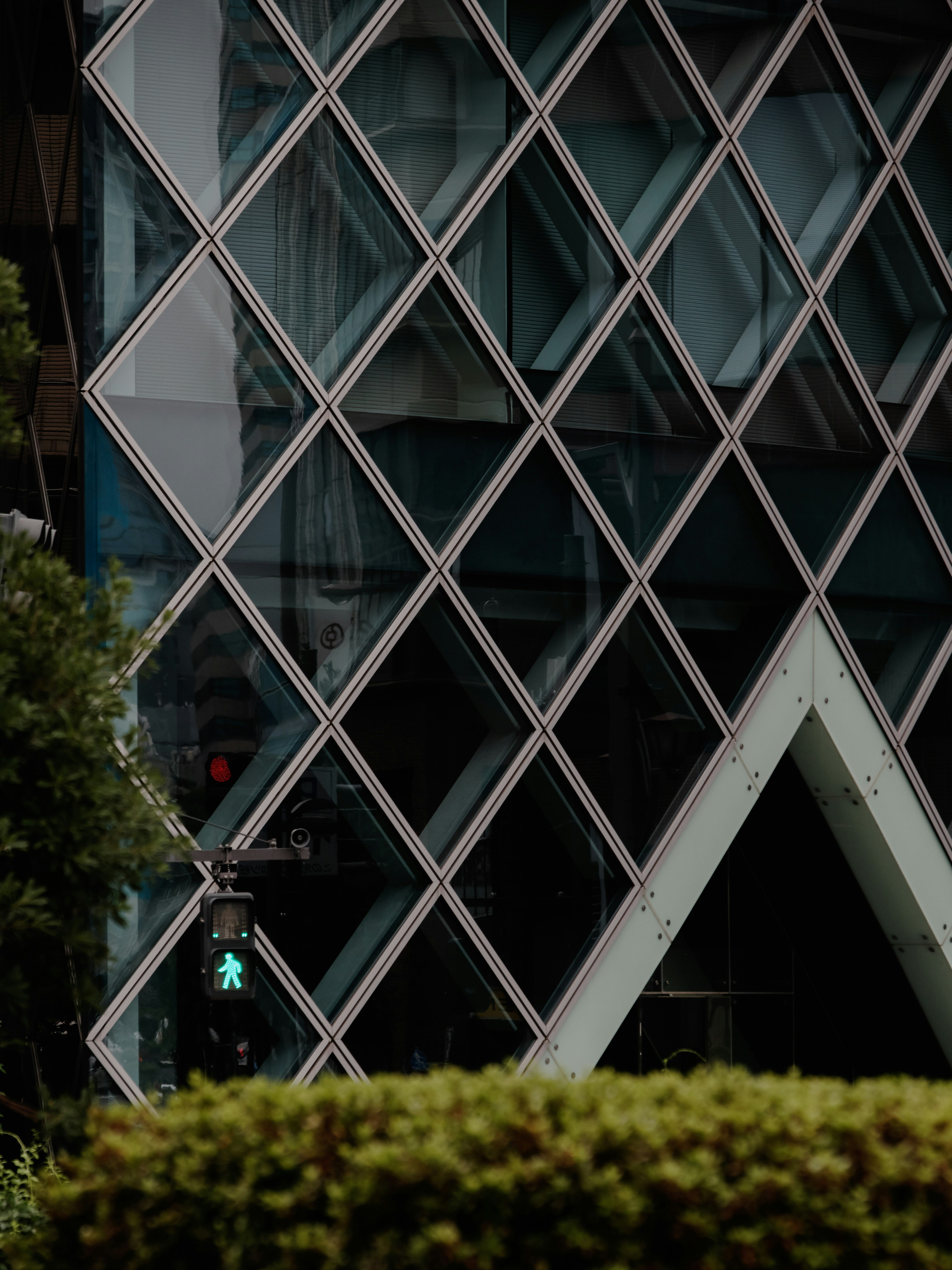 Part of a modern building with a diamond-shaped glass facade and a green traffic light