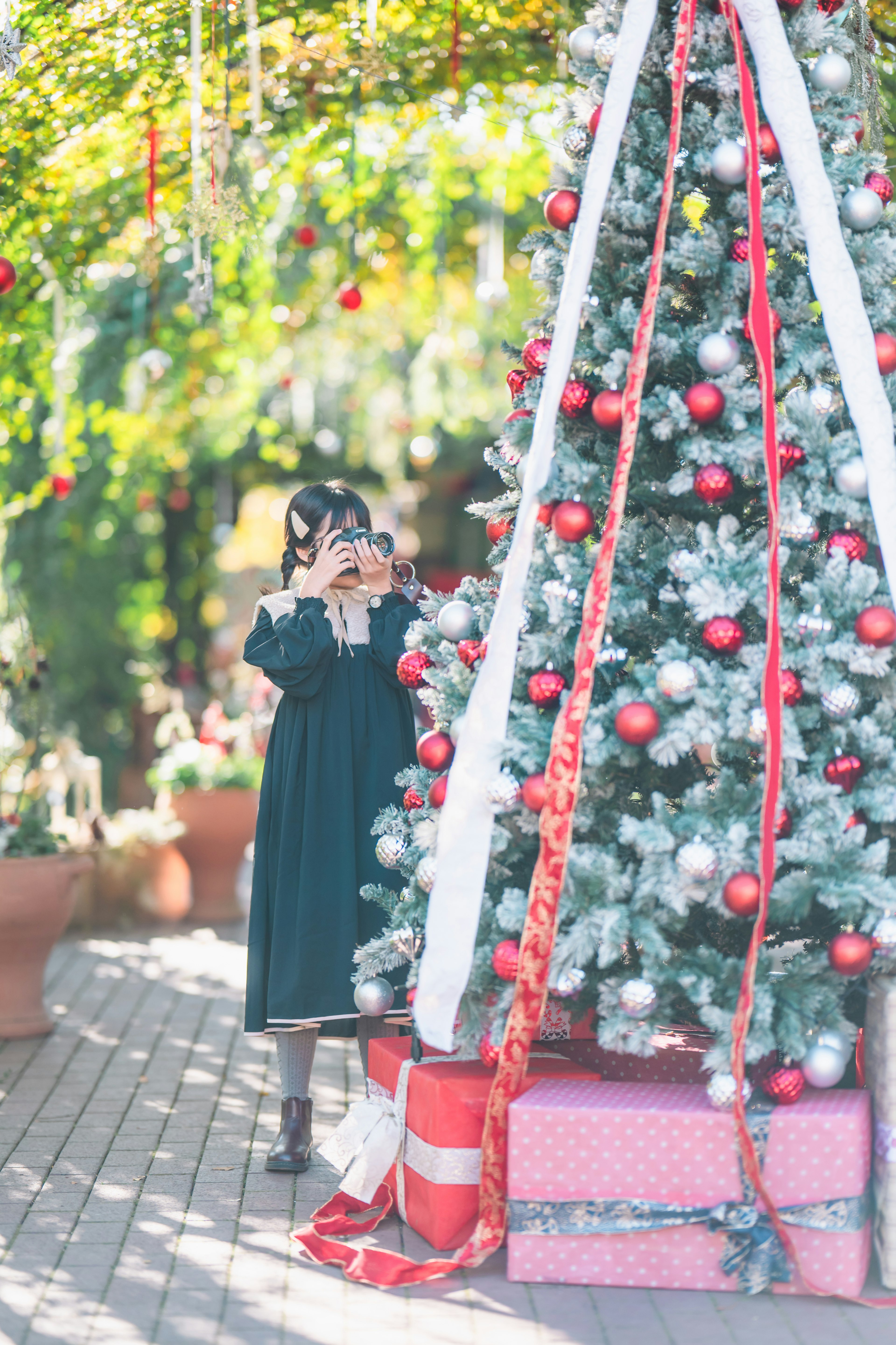 Ragazza in abito nero con nastri bianchi vicino a un albero di Natale decorato