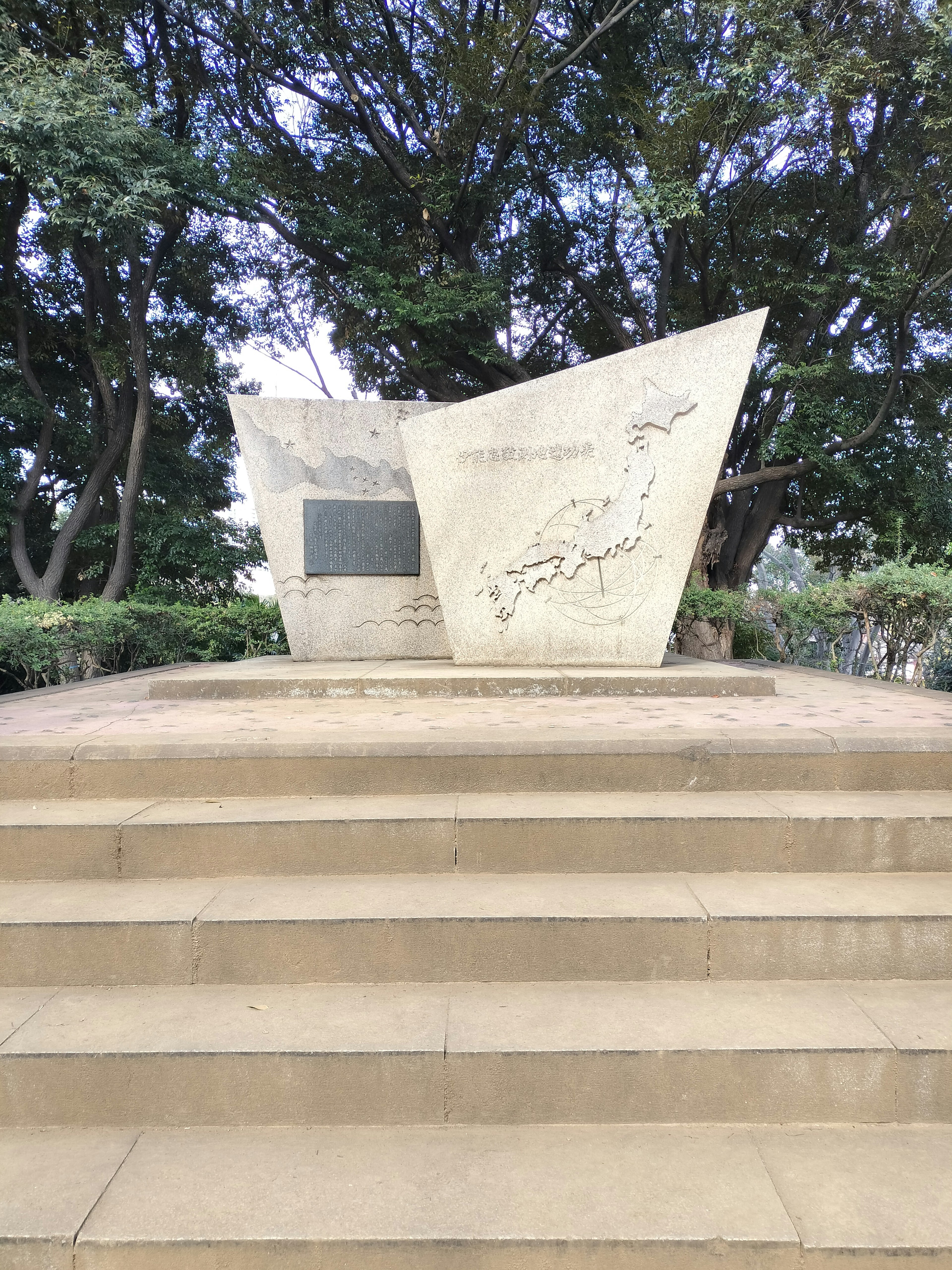 Modernes Steindenkmal auf Treppen umgeben von Bäumen