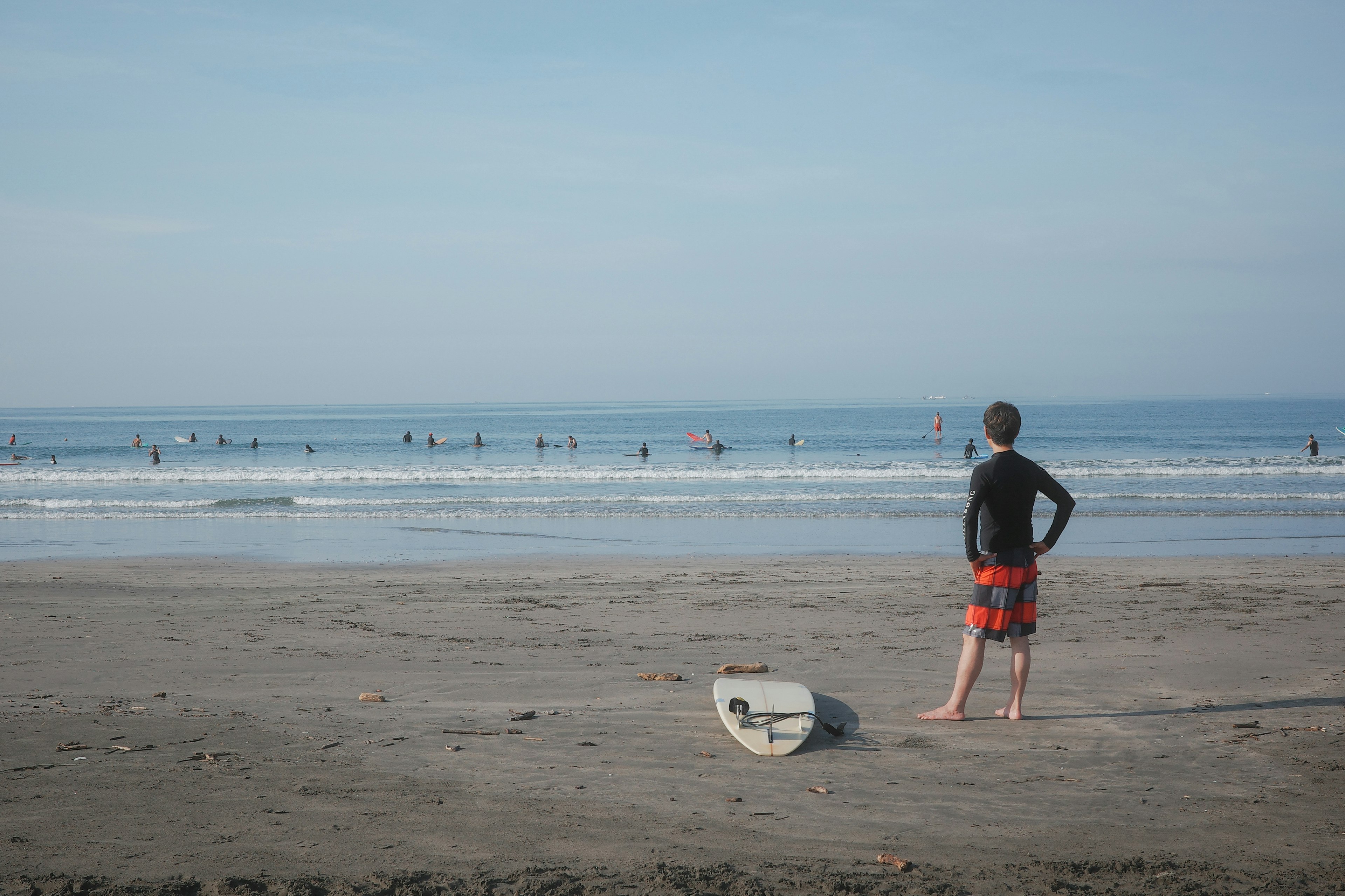 Garçon regardant l'océan avec une planche de surf à proximité