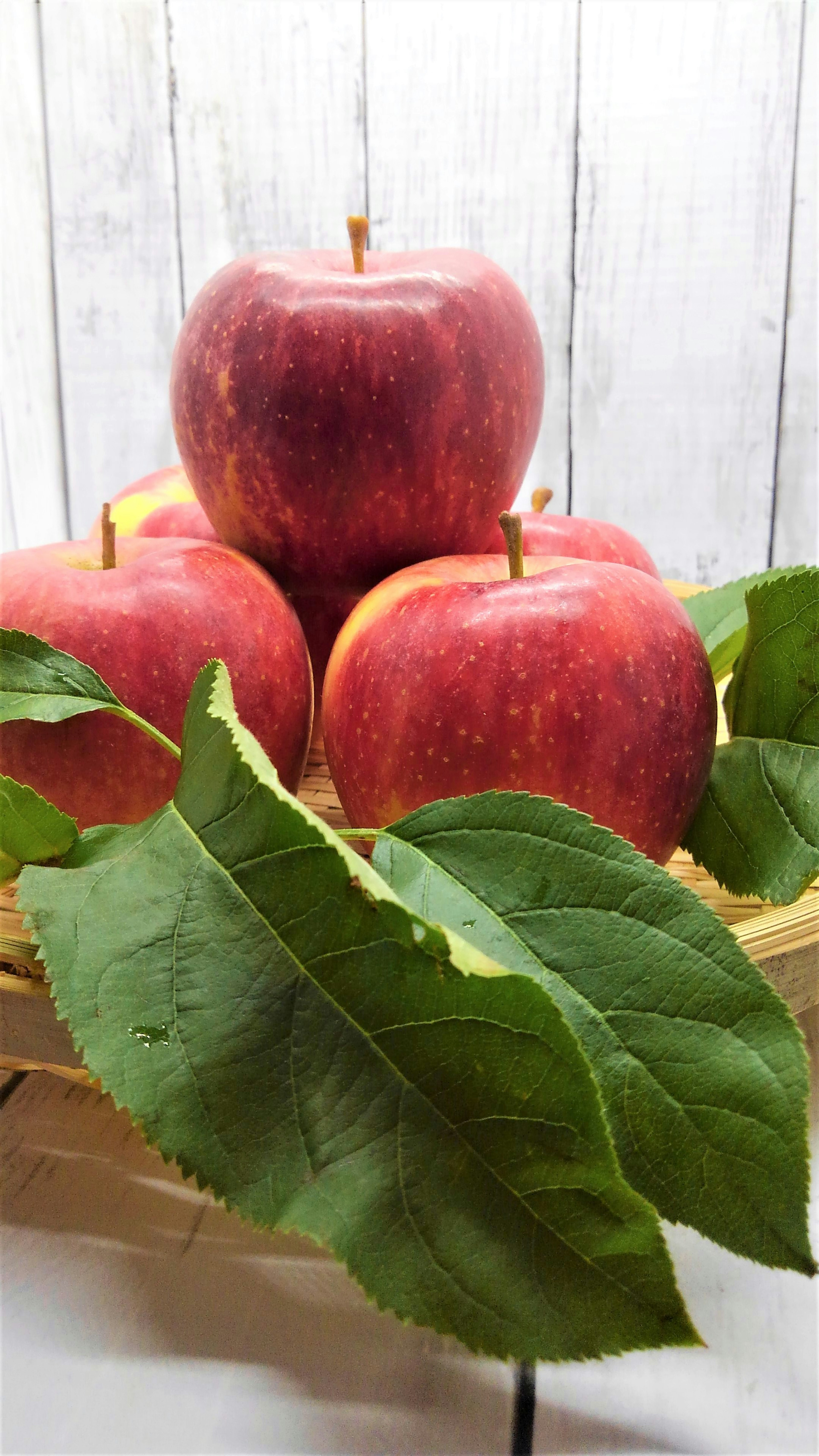 Red apples arranged in a bamboo basket with green leaves