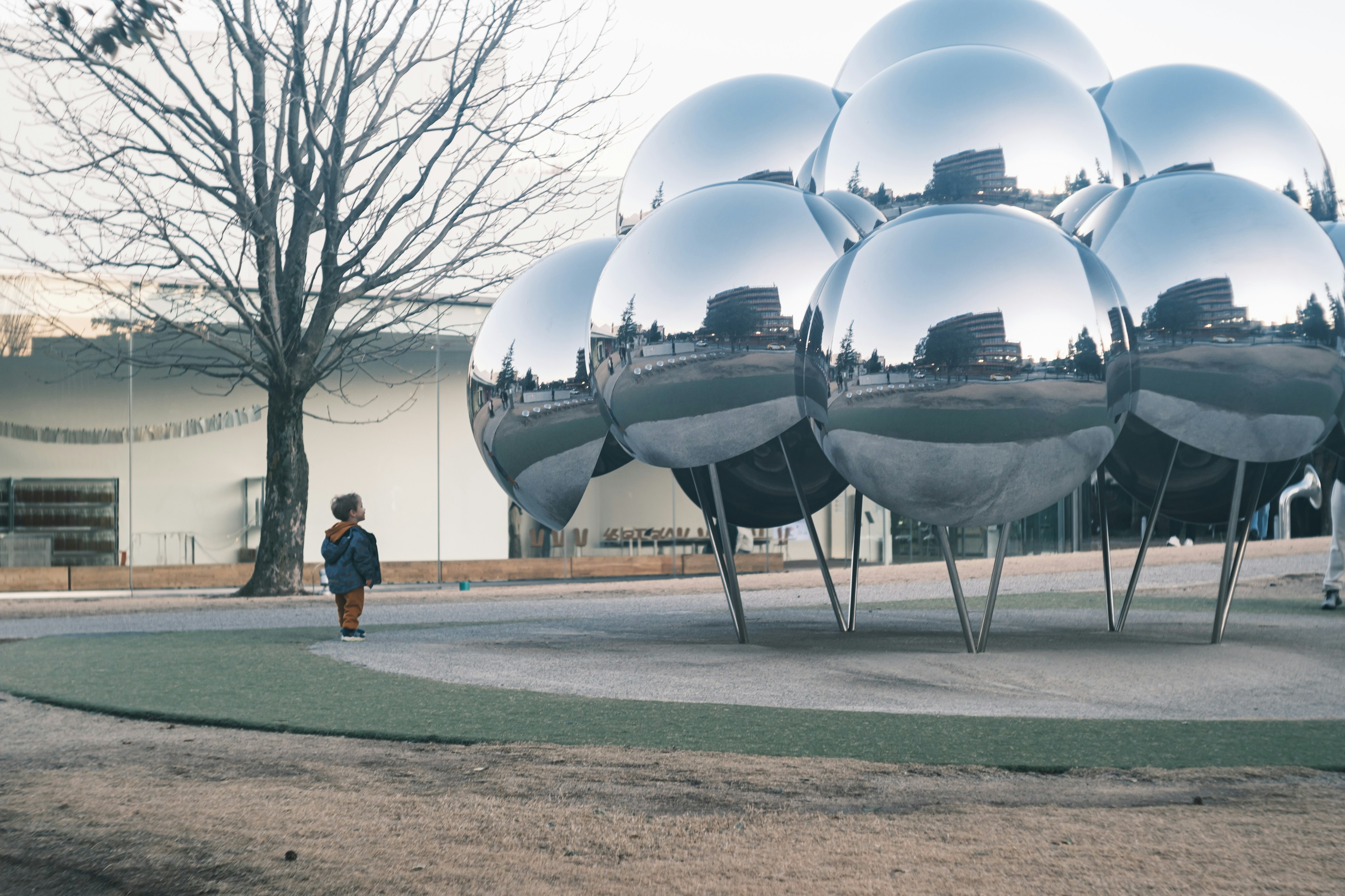 Un niño mirando una gran escultura esférica reflectante en un parque