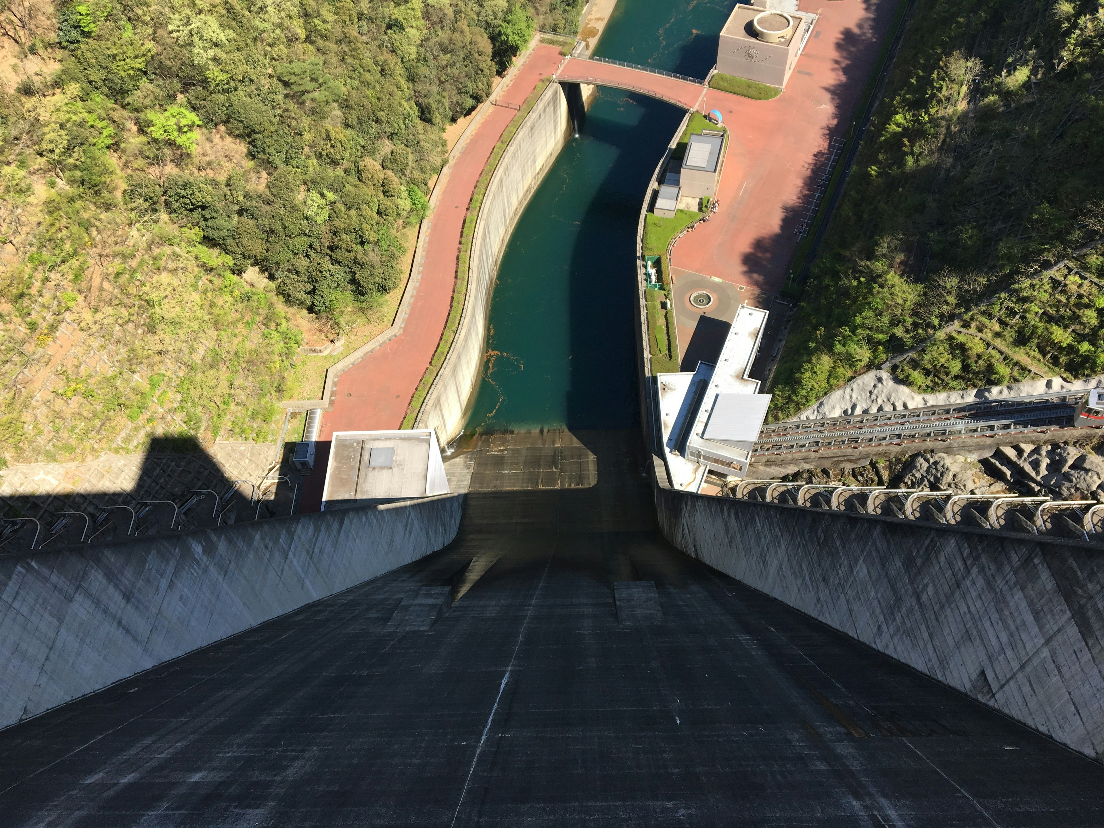 A view from the top of a dam overlooking a green landscape and a river