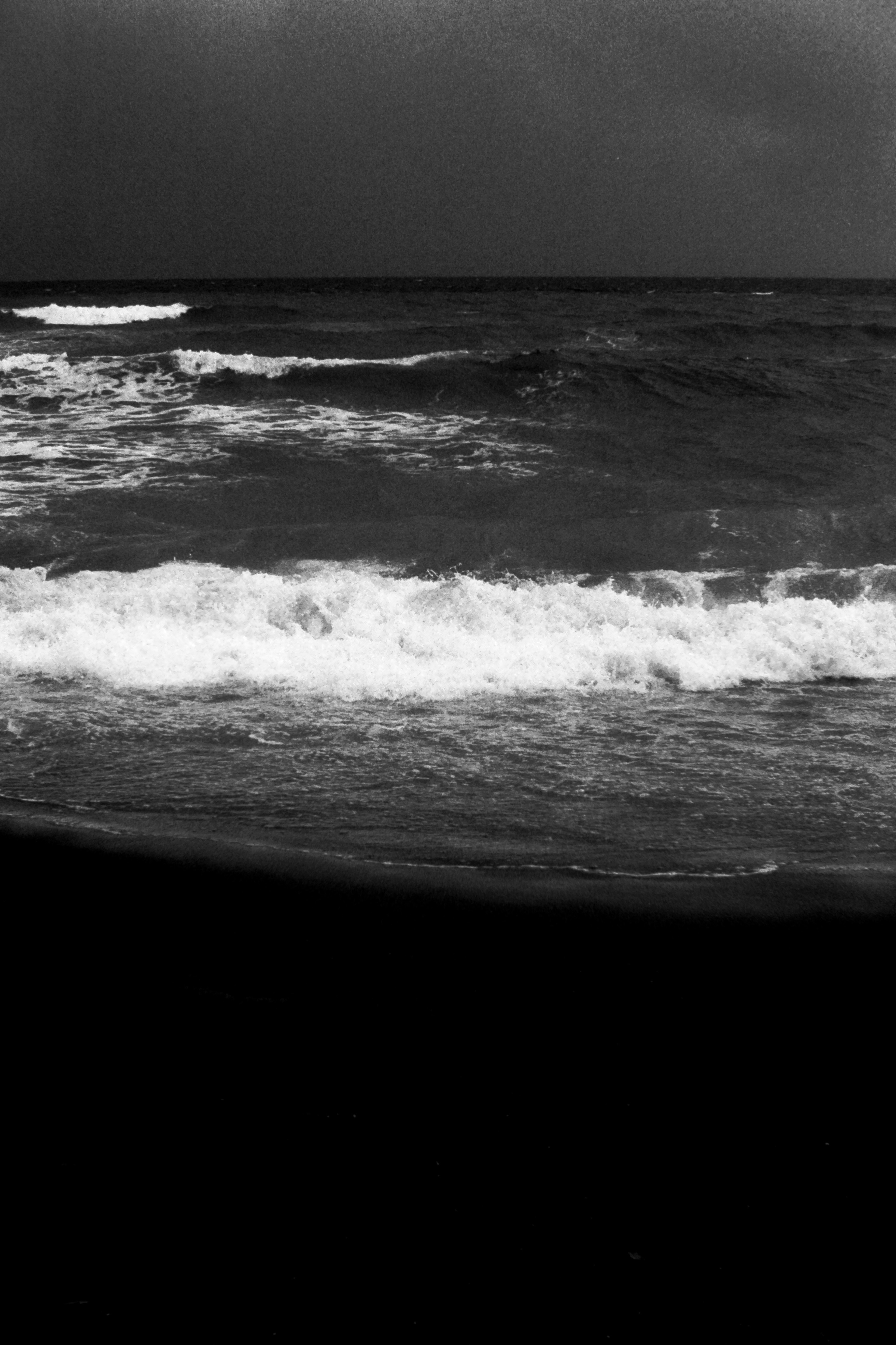 Waves crashing on a black sand beach with dark sky