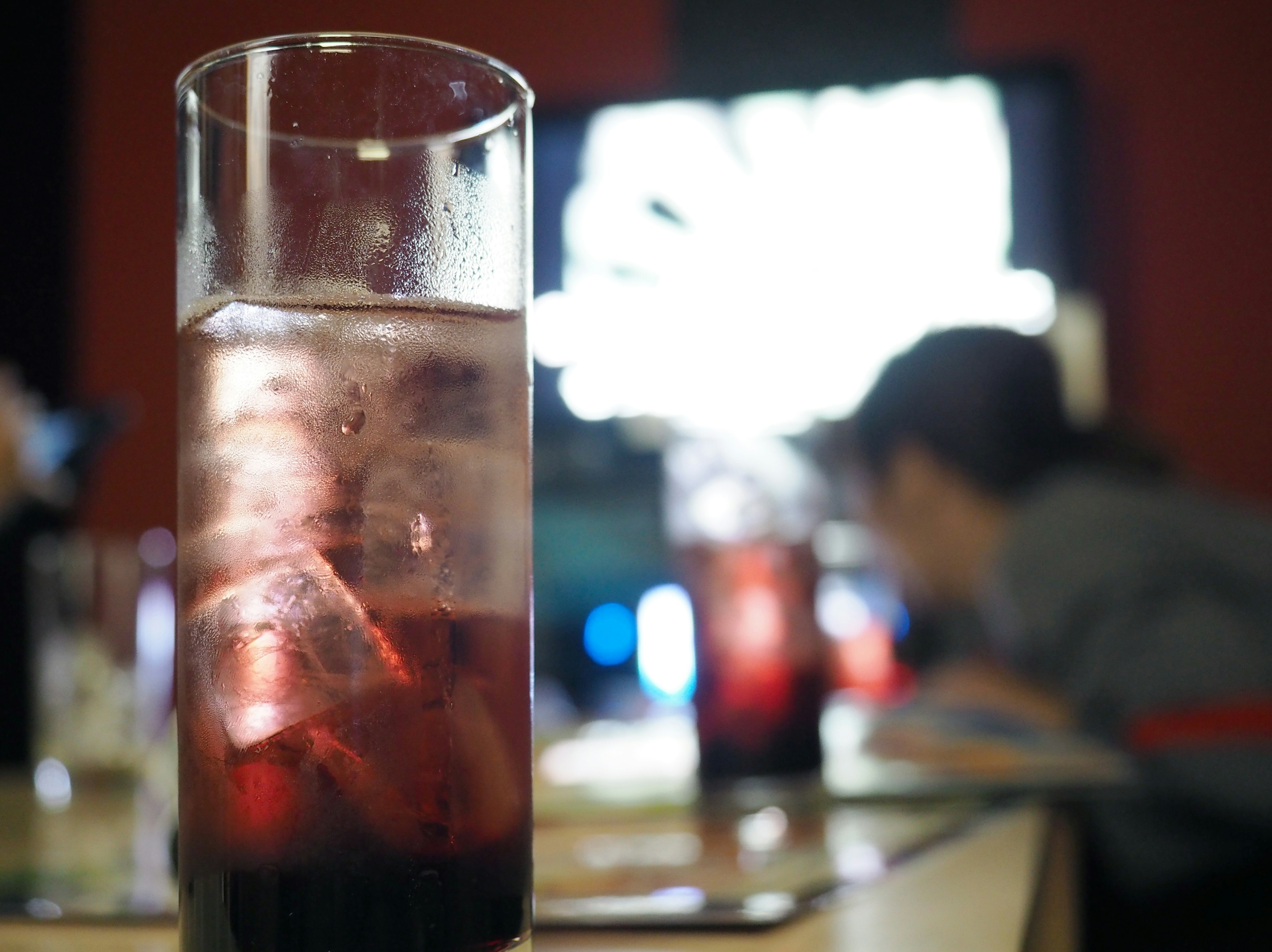 裝有冰塊的紅色飲料杯，背景模糊的人物