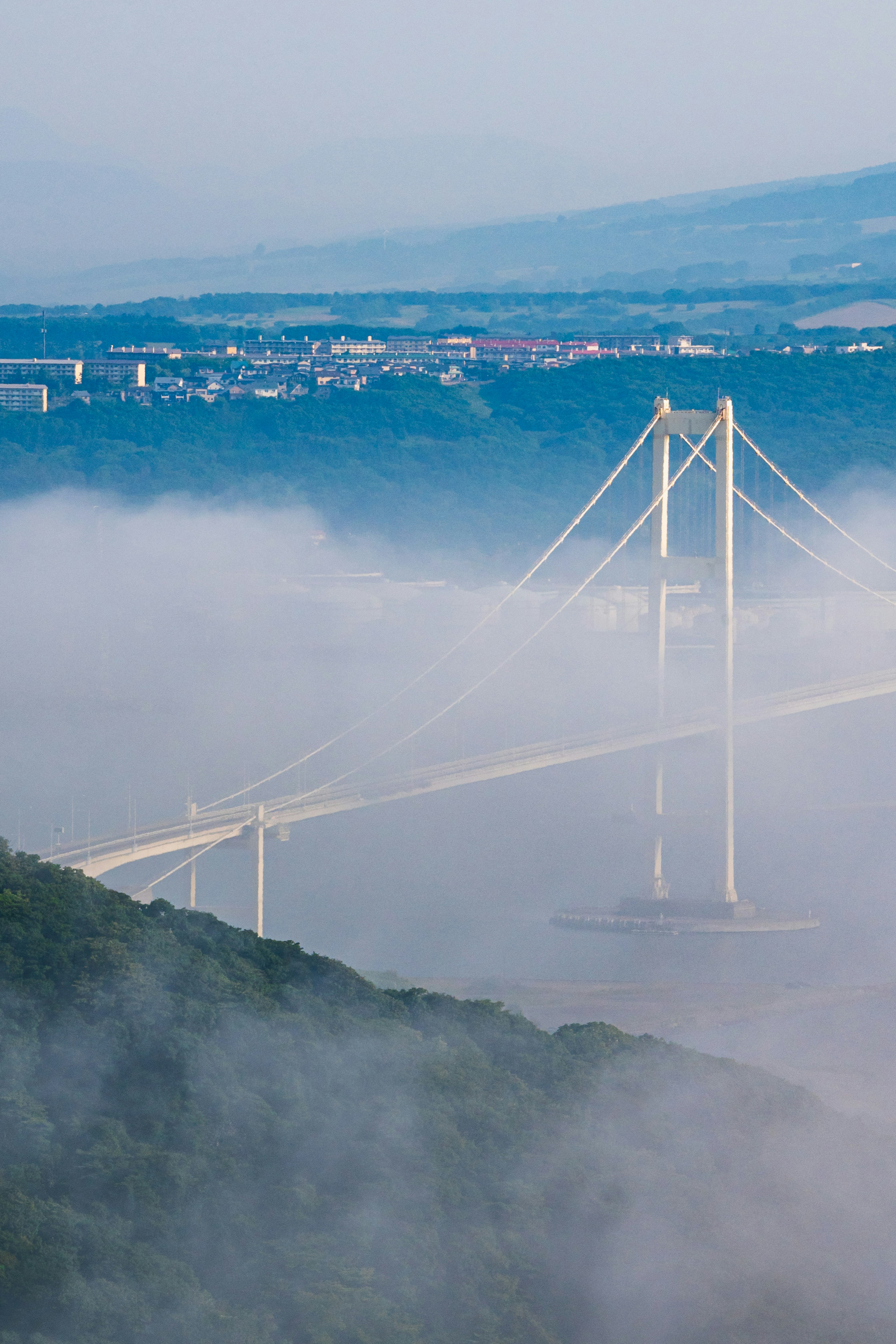 A beautiful bridge emerging from the fog with green mountains in the background