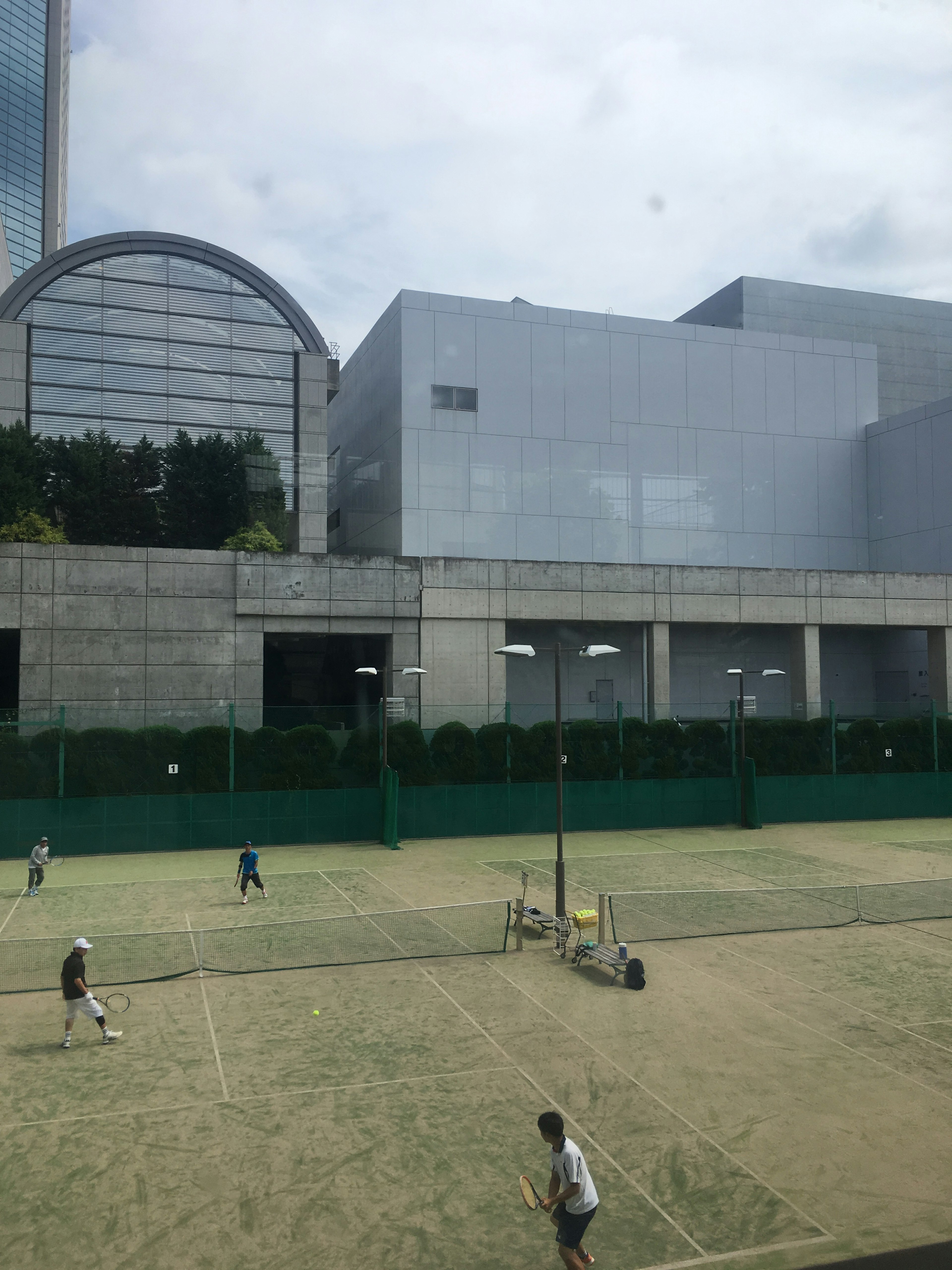 Blick auf Menschen, die Tennis auf einem Platz spielen, mit einem modernen Gebäude im Hintergrund