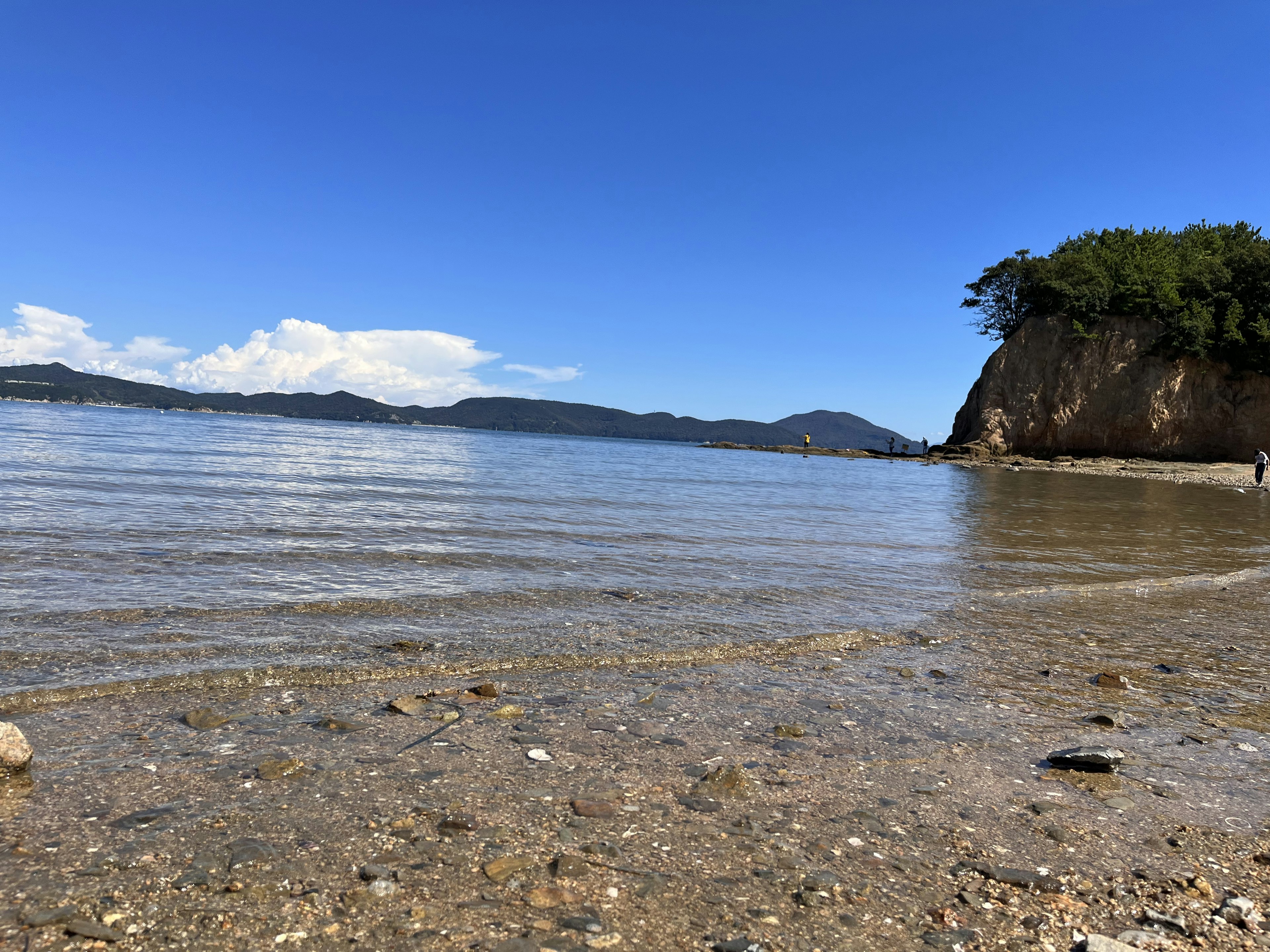 Scenic view of a calm beach with pebbles under a clear blue sky and distant mountains