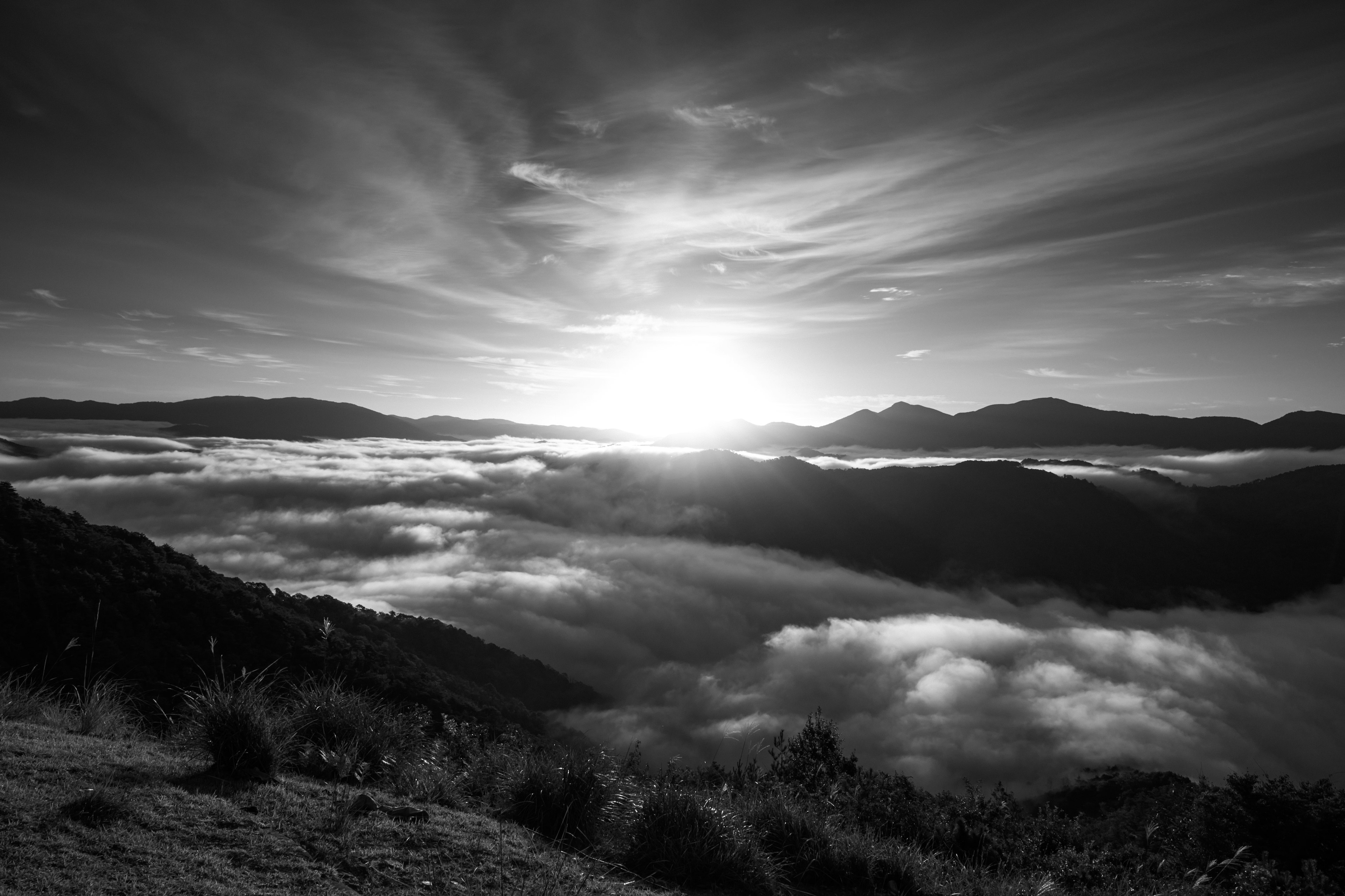 Schwarzweißbild der Sonne, die über nebligen Bergen aufgeht